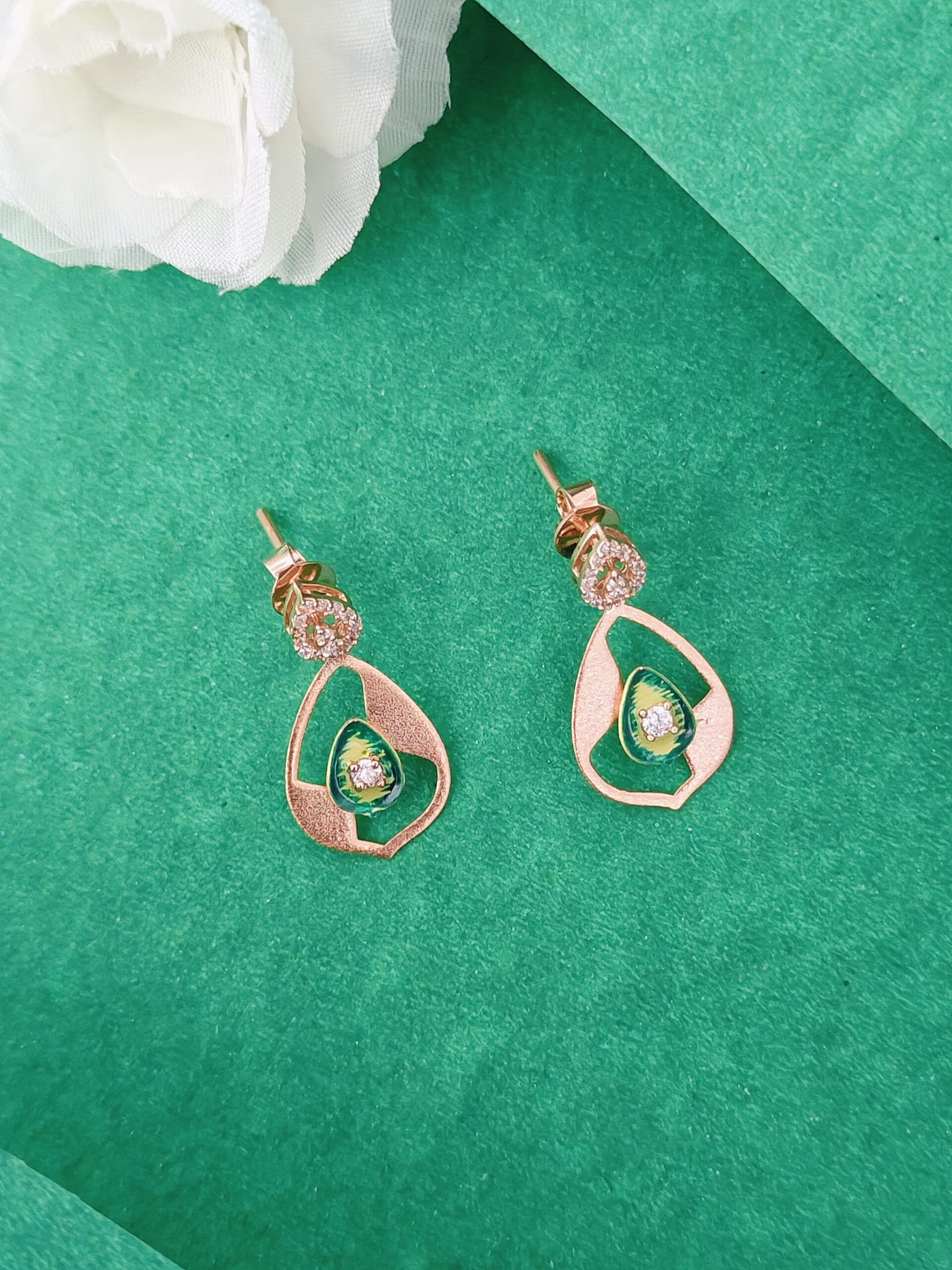 Pair of green and rose gold earrings on a green background with a white flower.