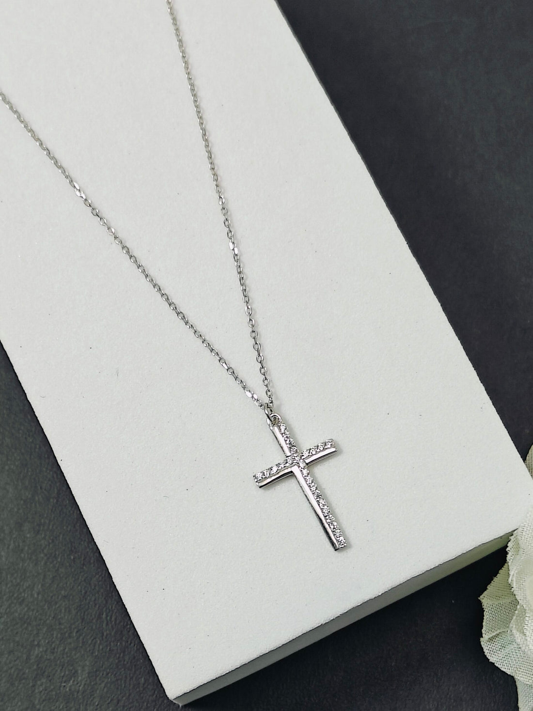 Silver cross necklace on a white box with a gray background