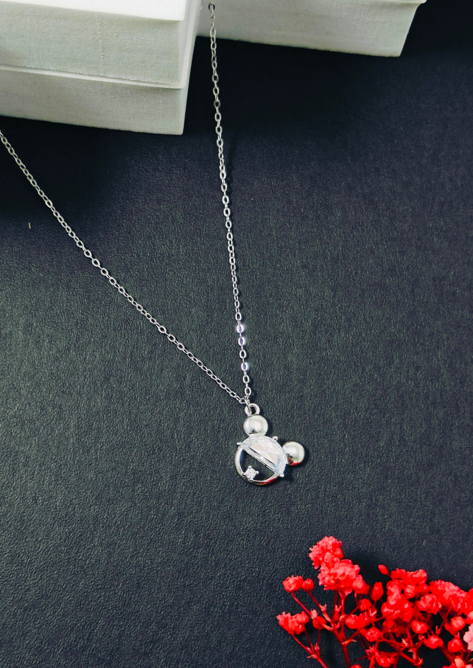 Silver necklace with a pendant on a dark surface with red flowers