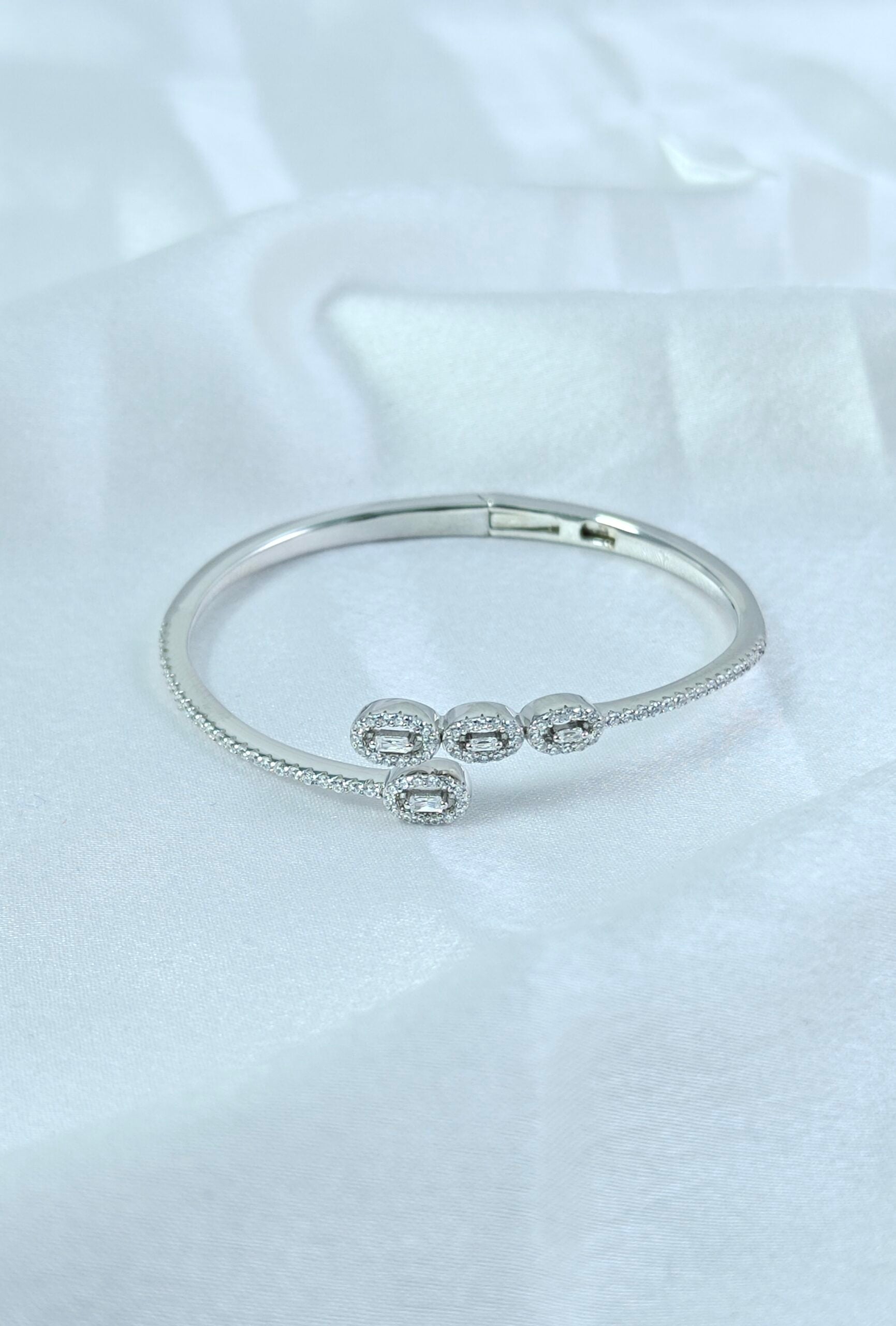 Silver bracelet with three round embellishments on a white fabric background