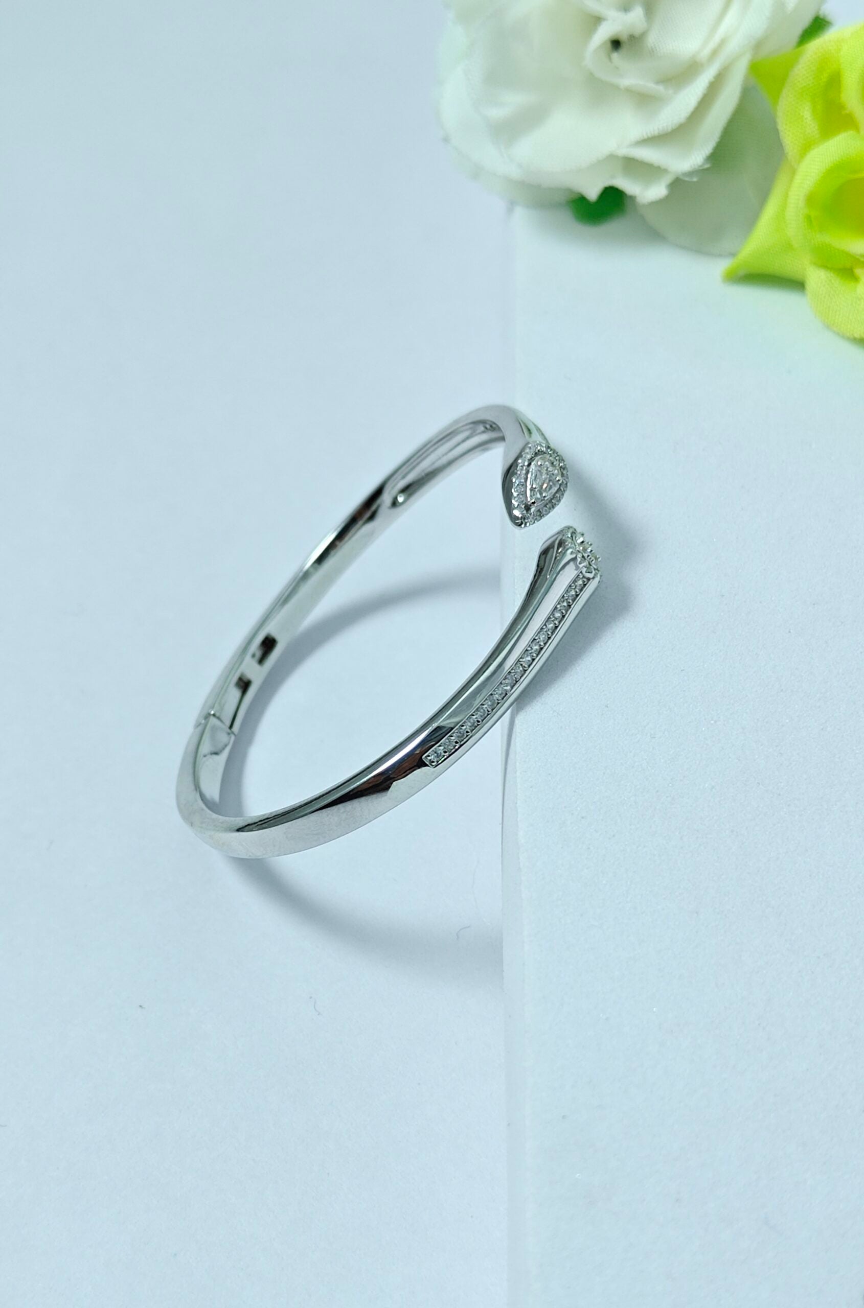 Silver bracelet on a light gray background with flowers in the corner