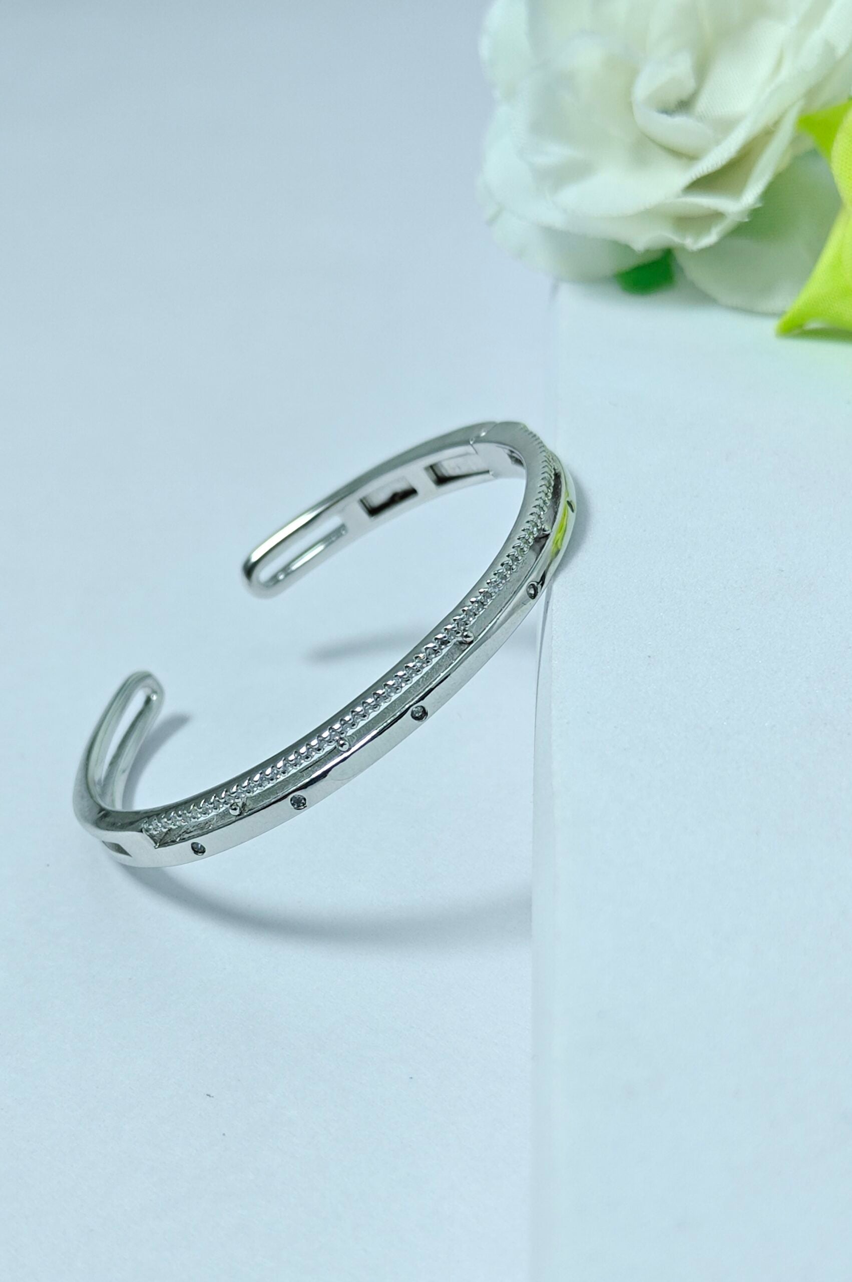 Silver bracelet with small stones on a light gray background with white roses.