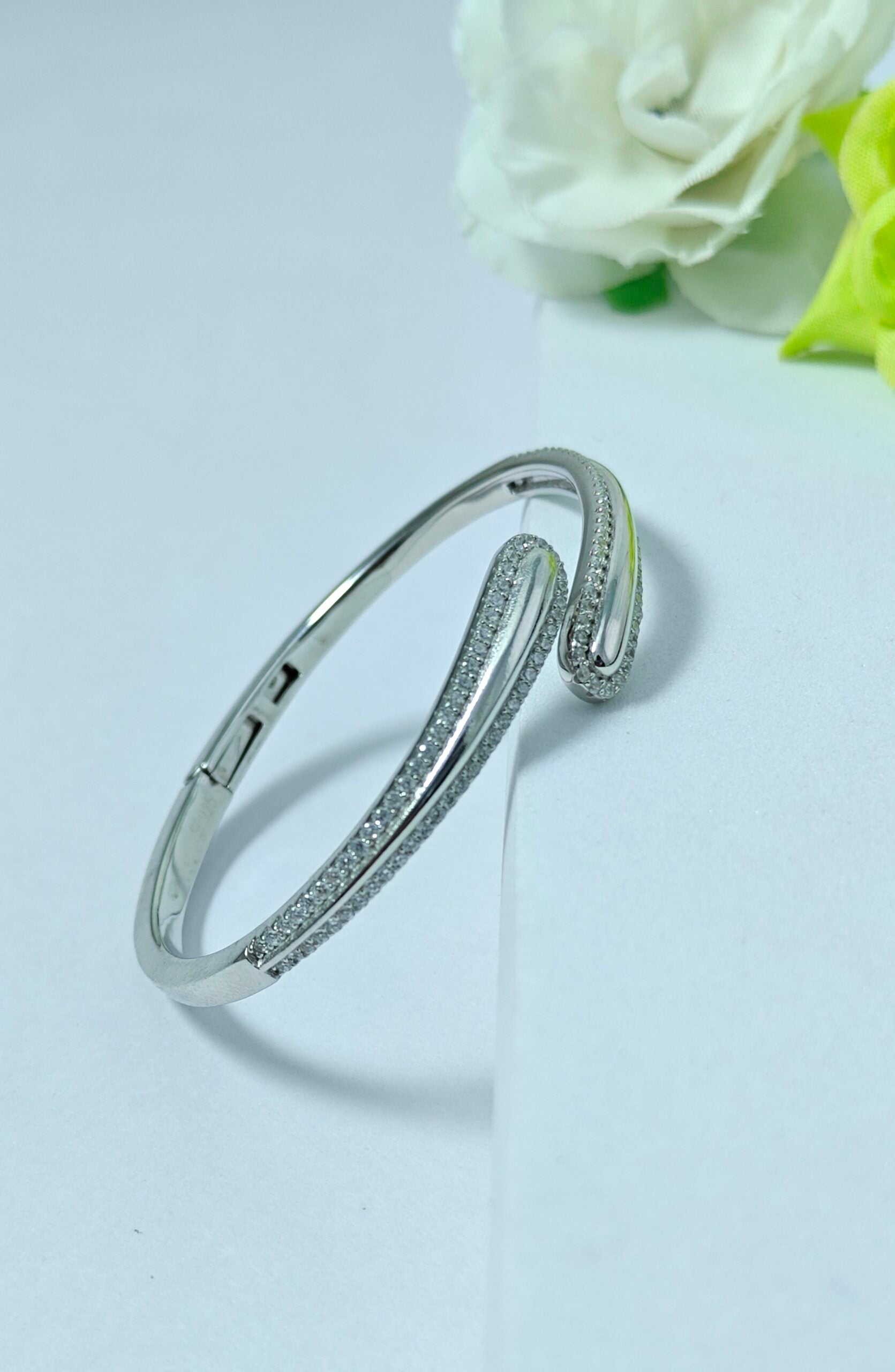 Silver bracelet with small stones on a light gray background with white roses.