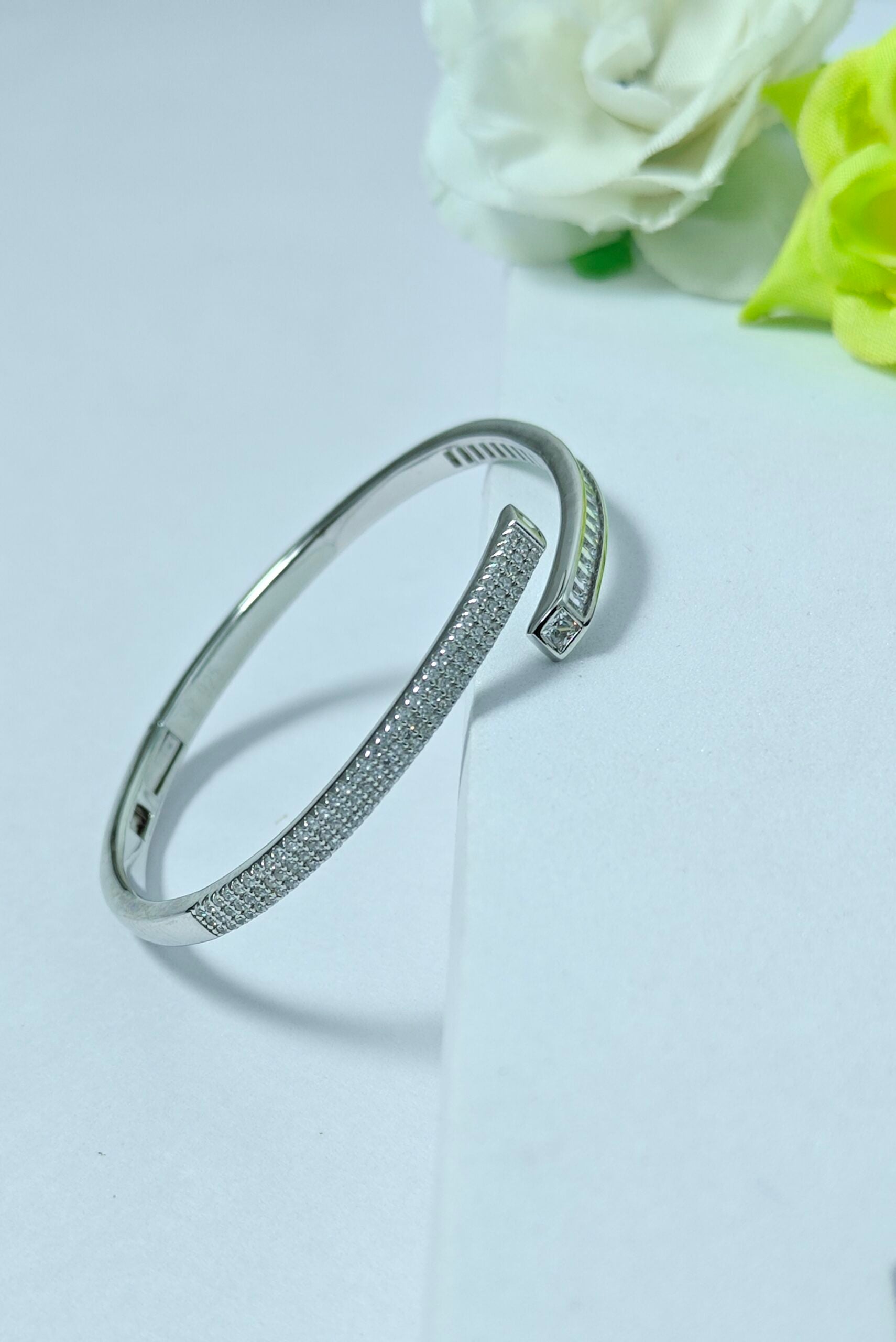 Silver bracelet with clear stones on a light gray background with flowers.