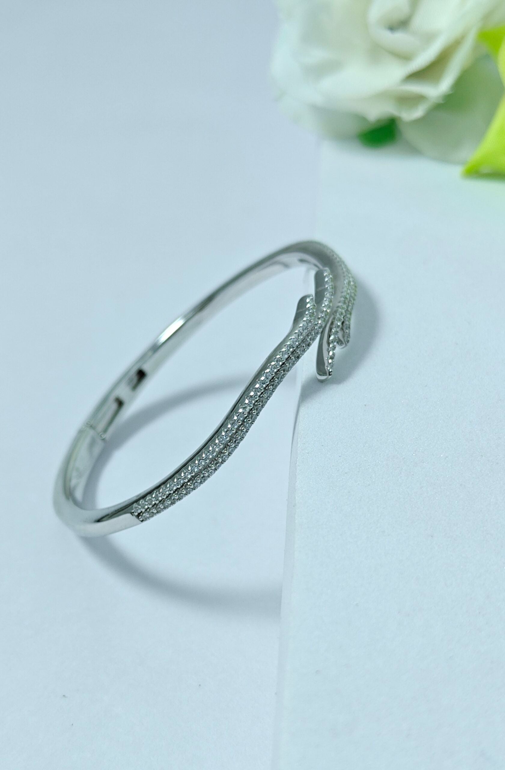 Silver bracelet on a light gray background with a white rose.