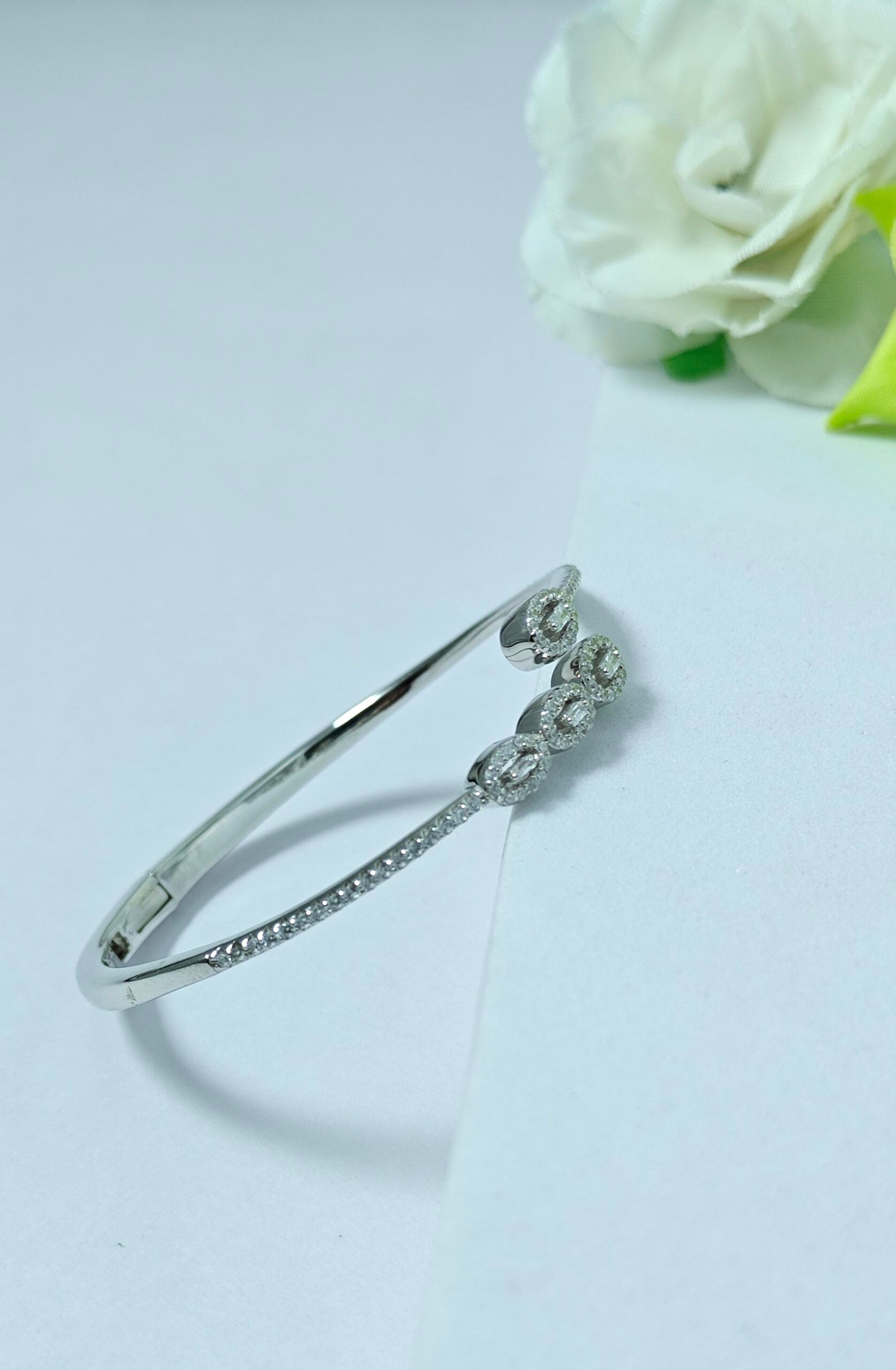 Silver bracelet with floral design on a light gray background with a white rose.