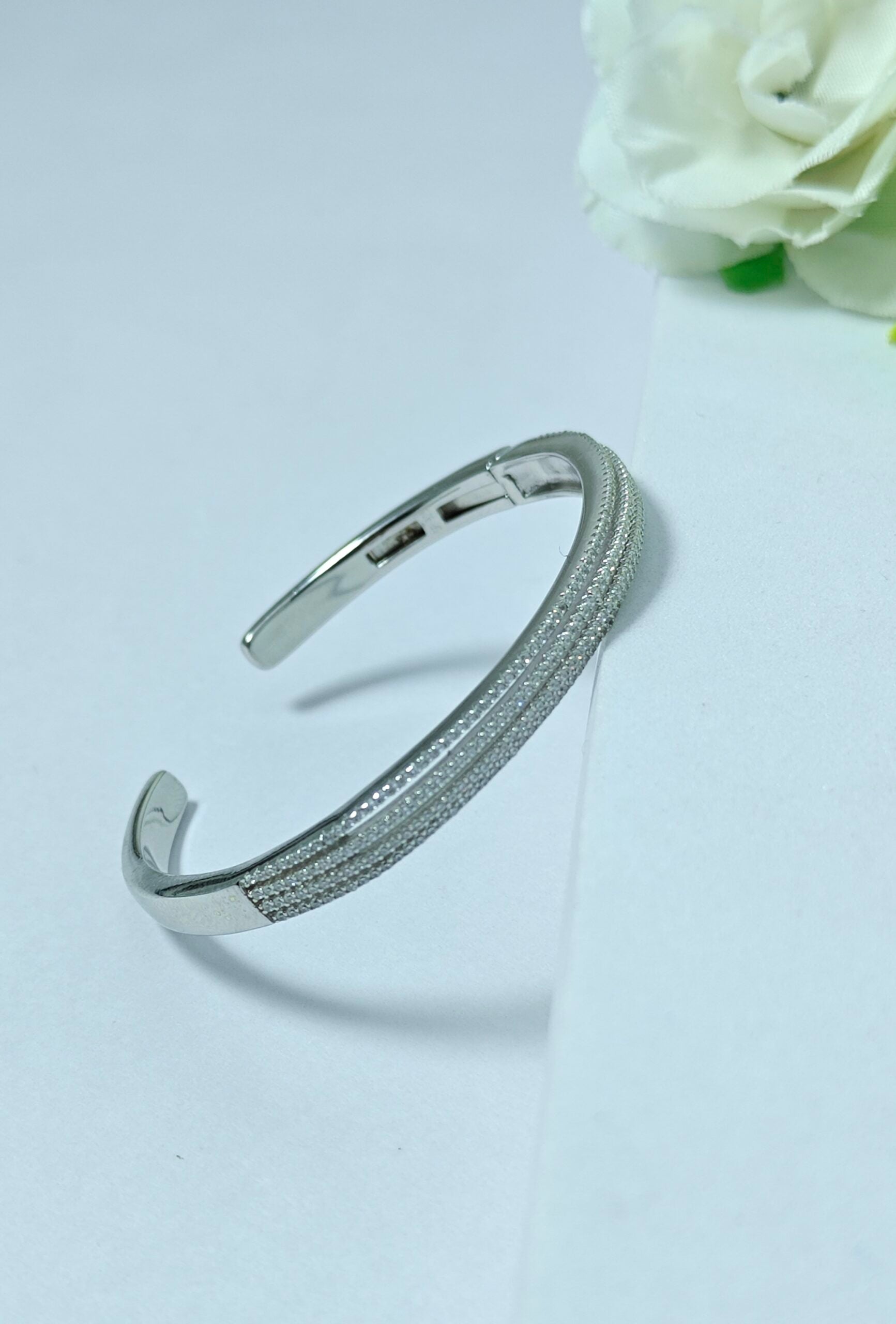 Silver bracelet on a light gray background with a white flower.