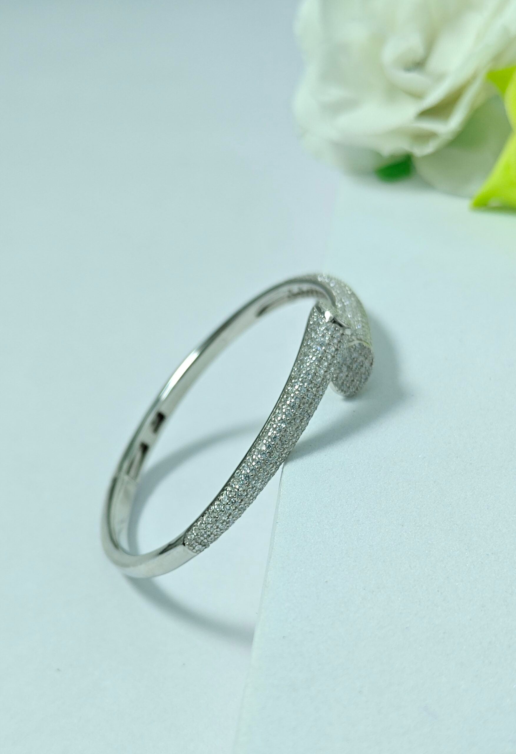 Silver bracelet on a light gray background with a white rose.