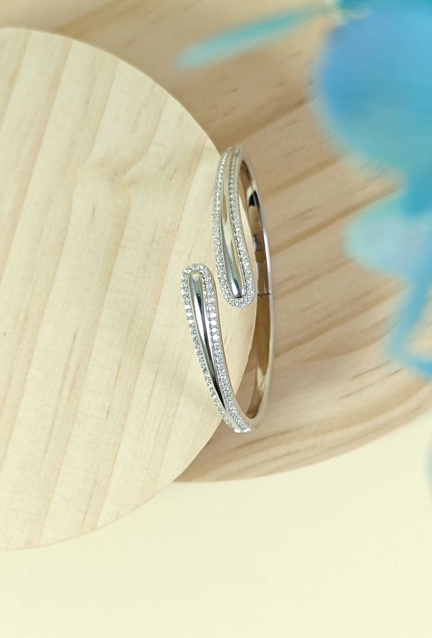 Two silver hoop earrings on a wooden surface with a blurred blue background