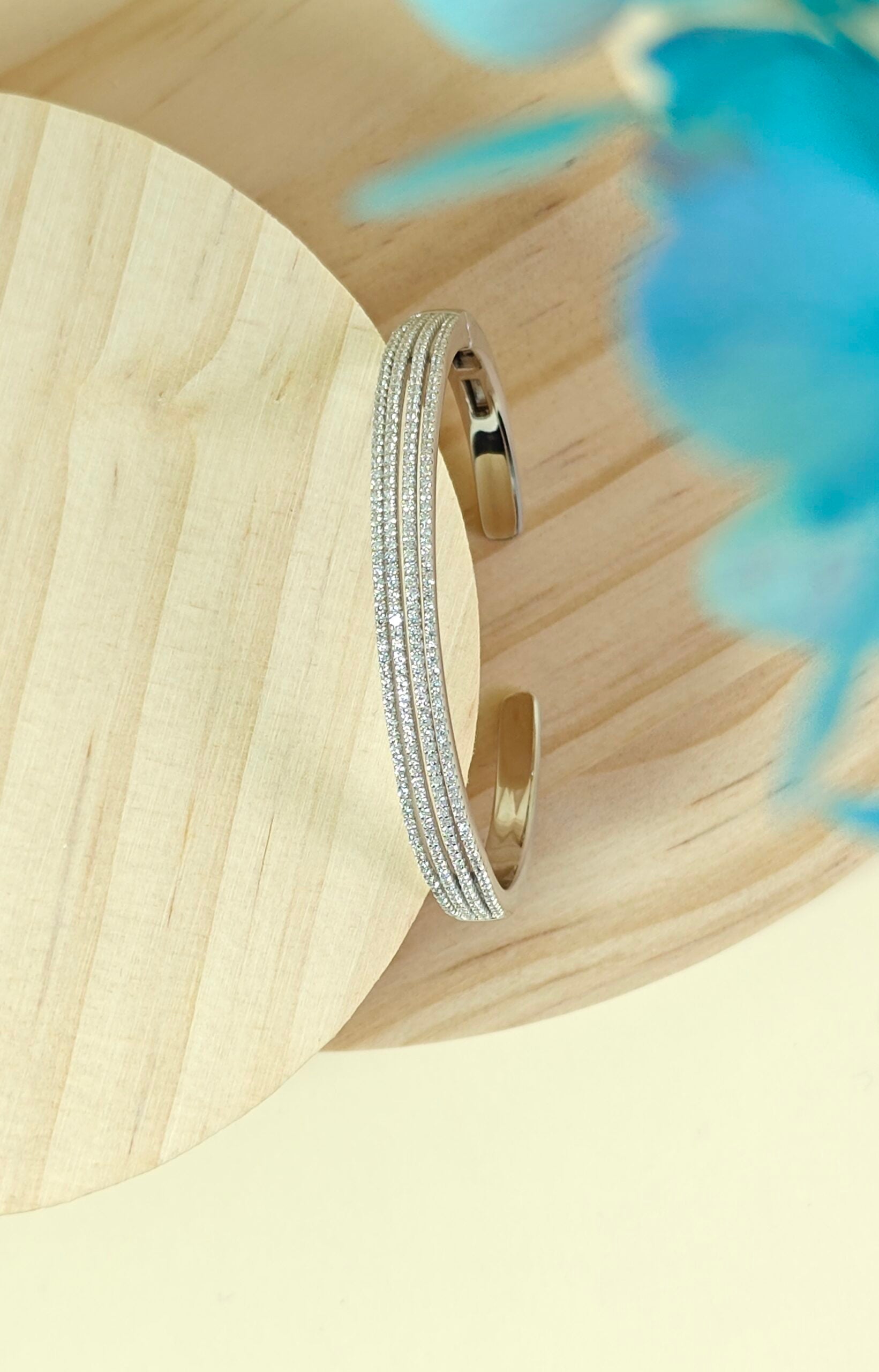 Gold bracelet on a wooden surface with a blurred blue flower in the background