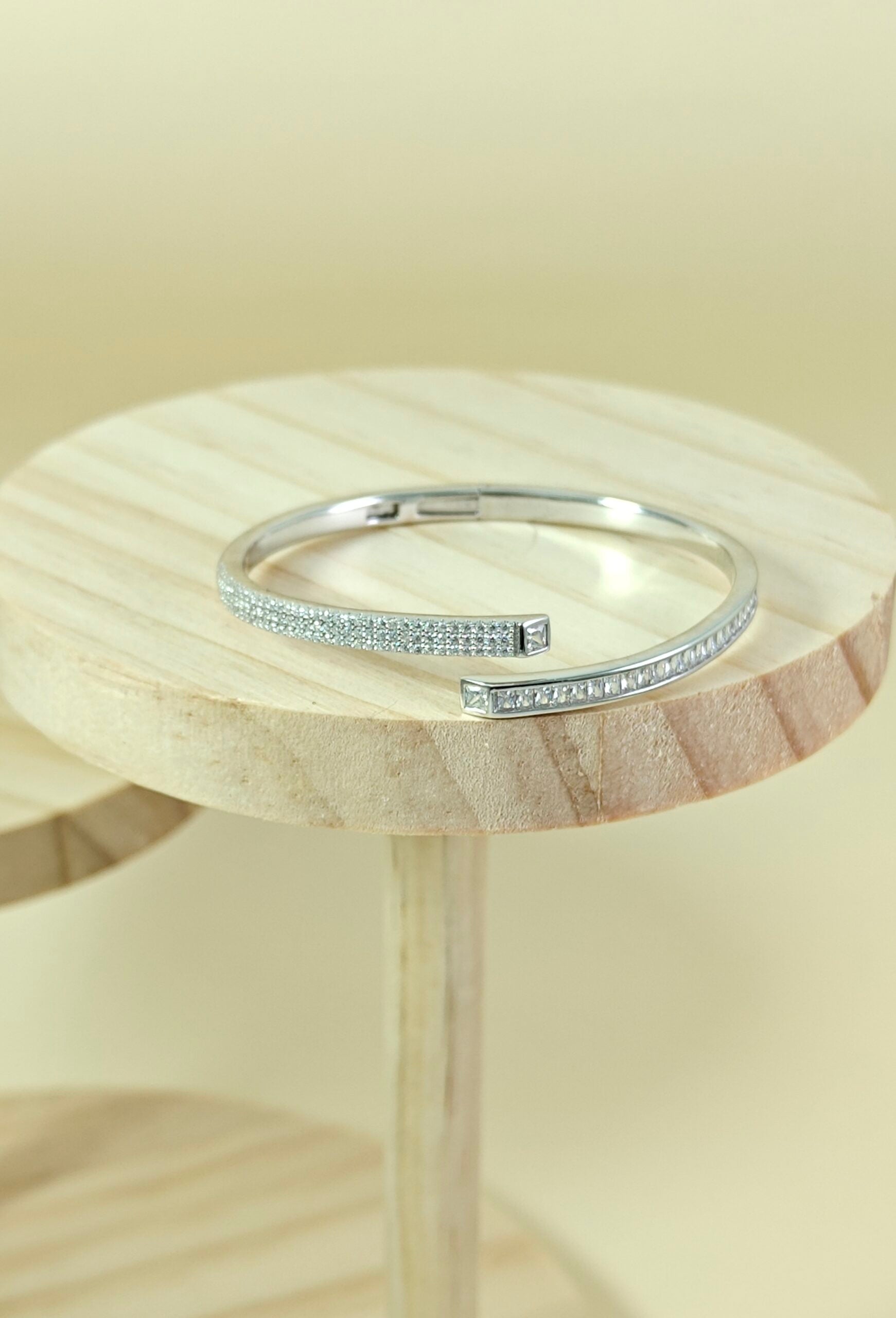Silver ring with small stones on a wooden stand against a beige background