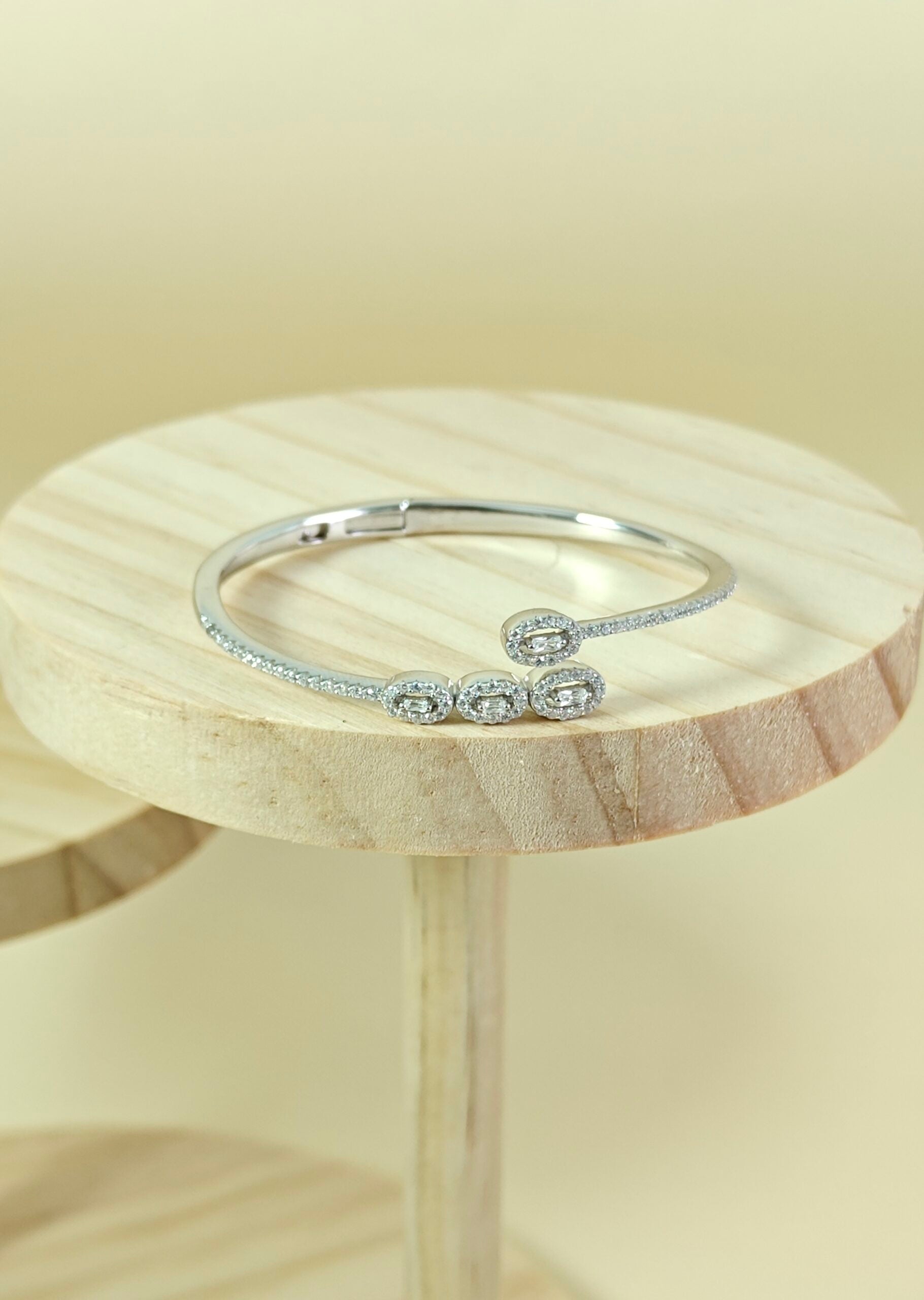 Silver bracelet with intricate design on a wooden stand against a beige background