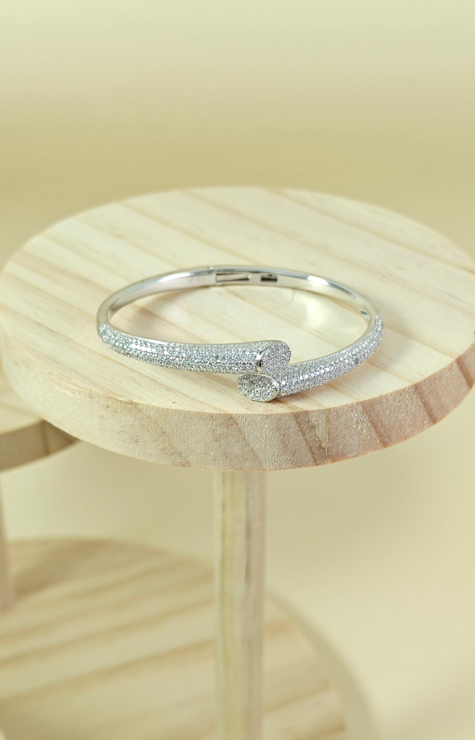 Silver bracelet with small stones on a wooden stand against a beige background