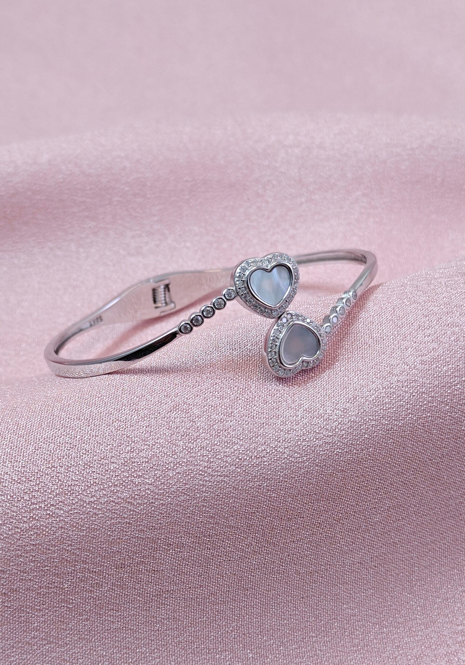 Silver bracelet with heart-shaped charms on a pink satin background