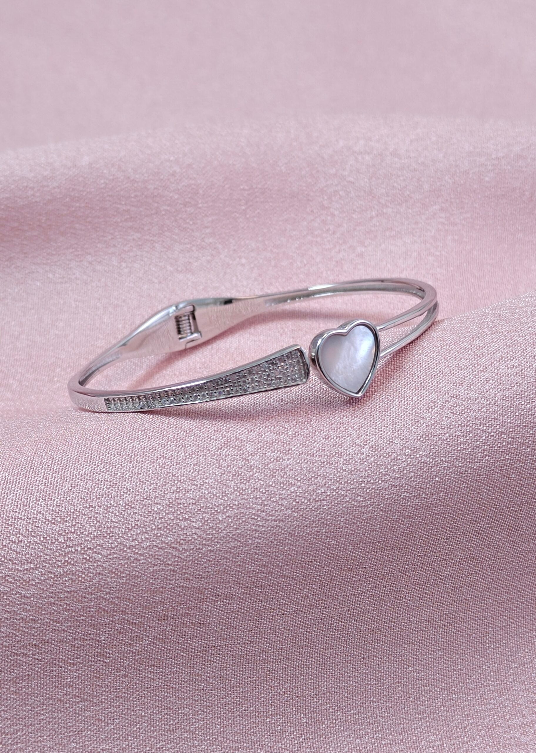 Silver bracelet with a heart-shaped gemstone on a pink background