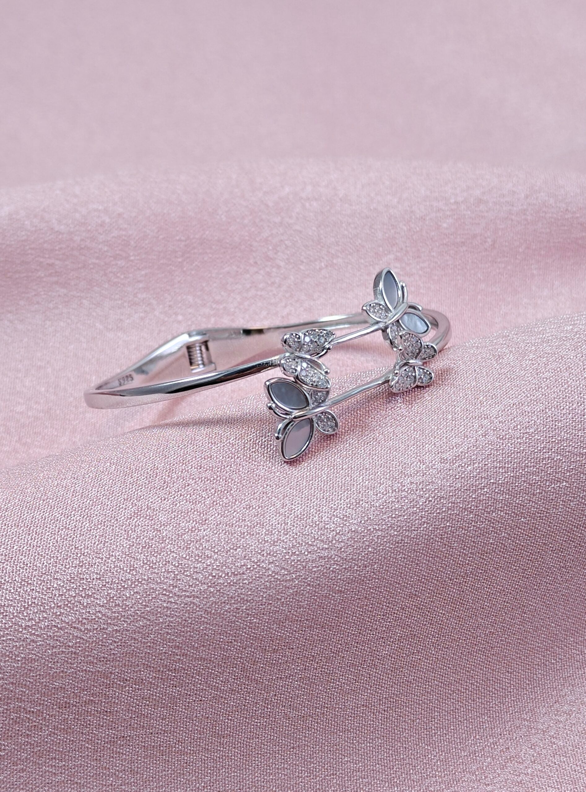 Silver hair clip with butterfly design on a pink satin background