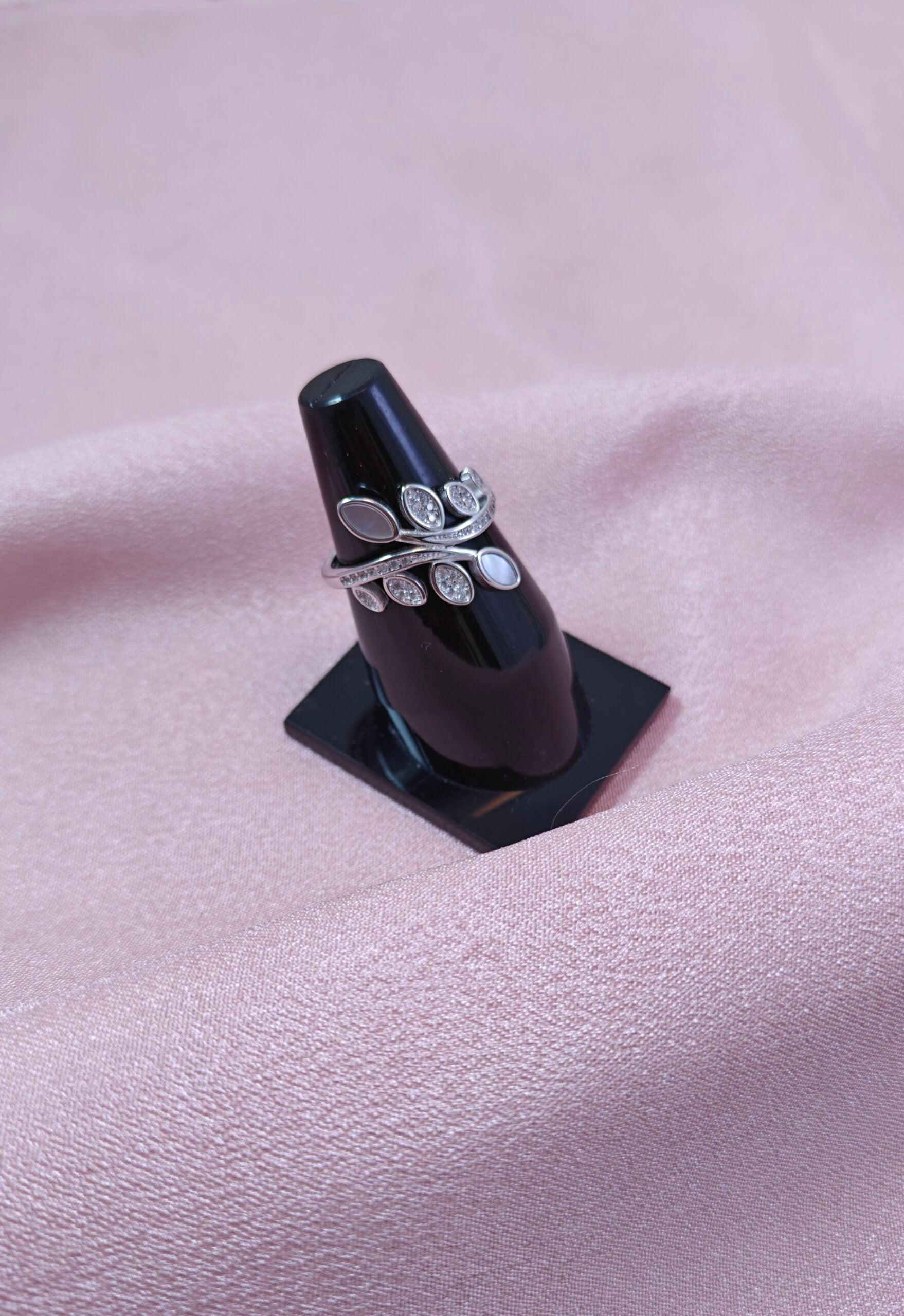 Silver ring with floral design on a black stand against a pink fabric background