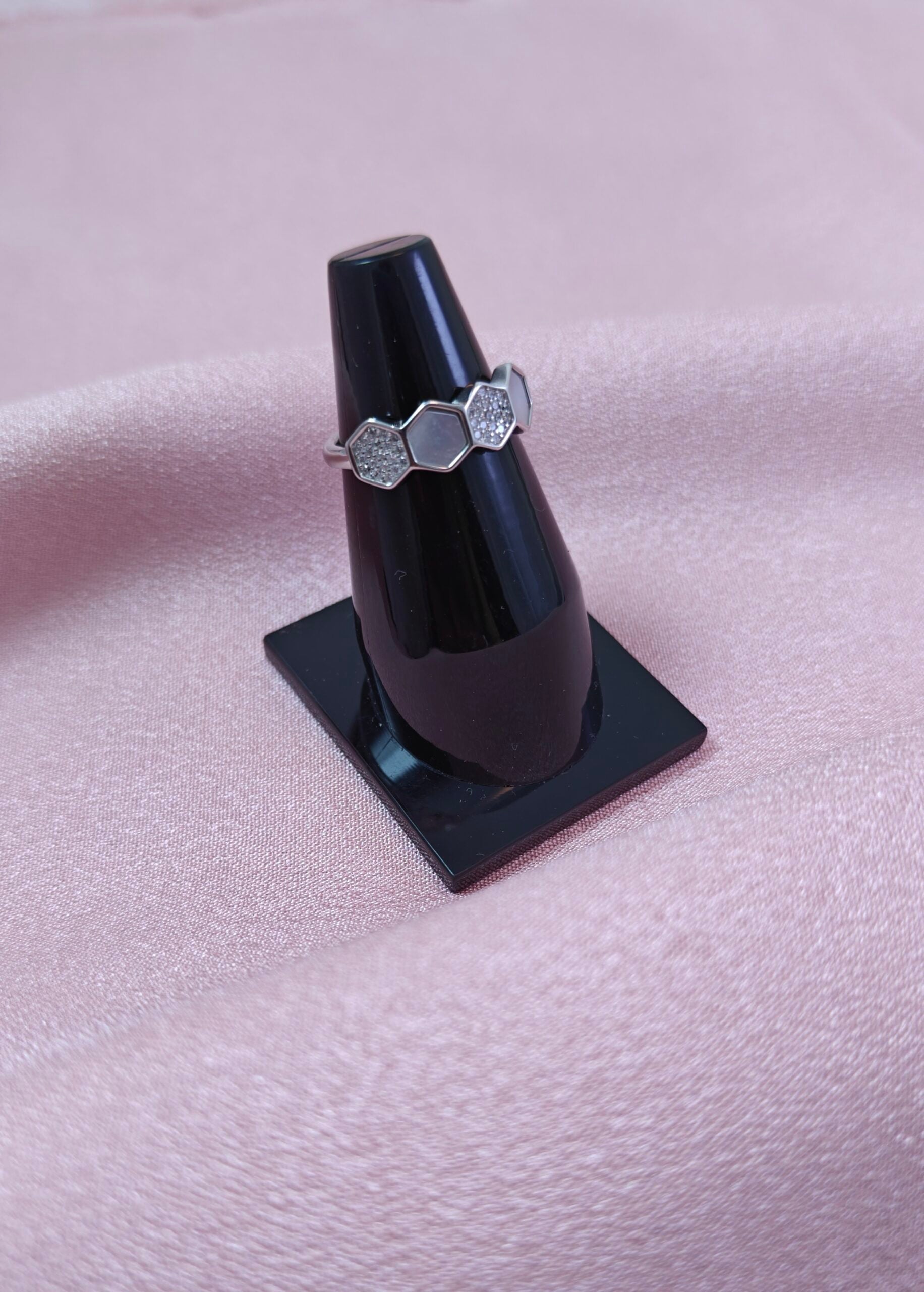 Silver ring on a black stand against a pink fabric background