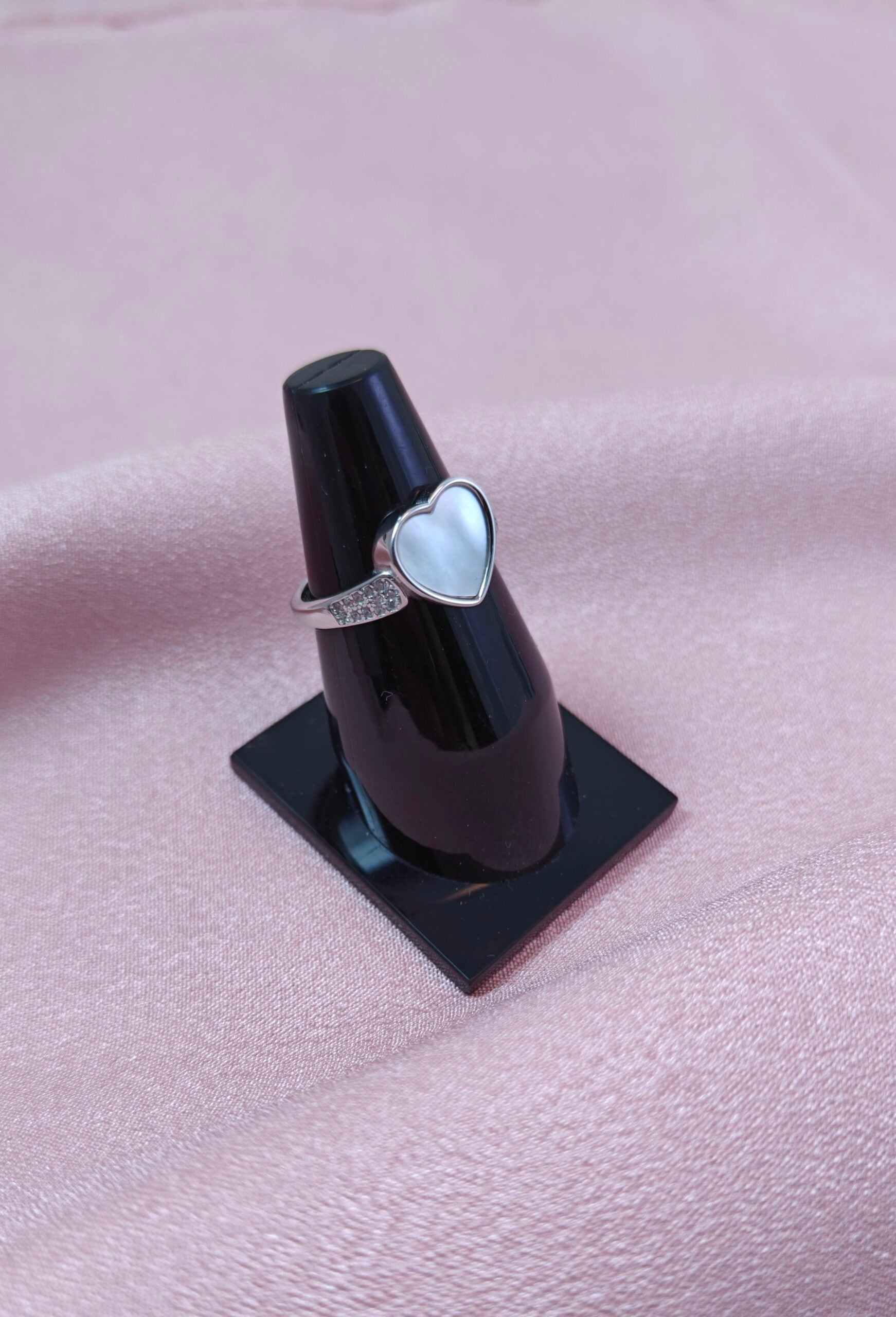 Heart-shaped ring on a black stand against a pink background