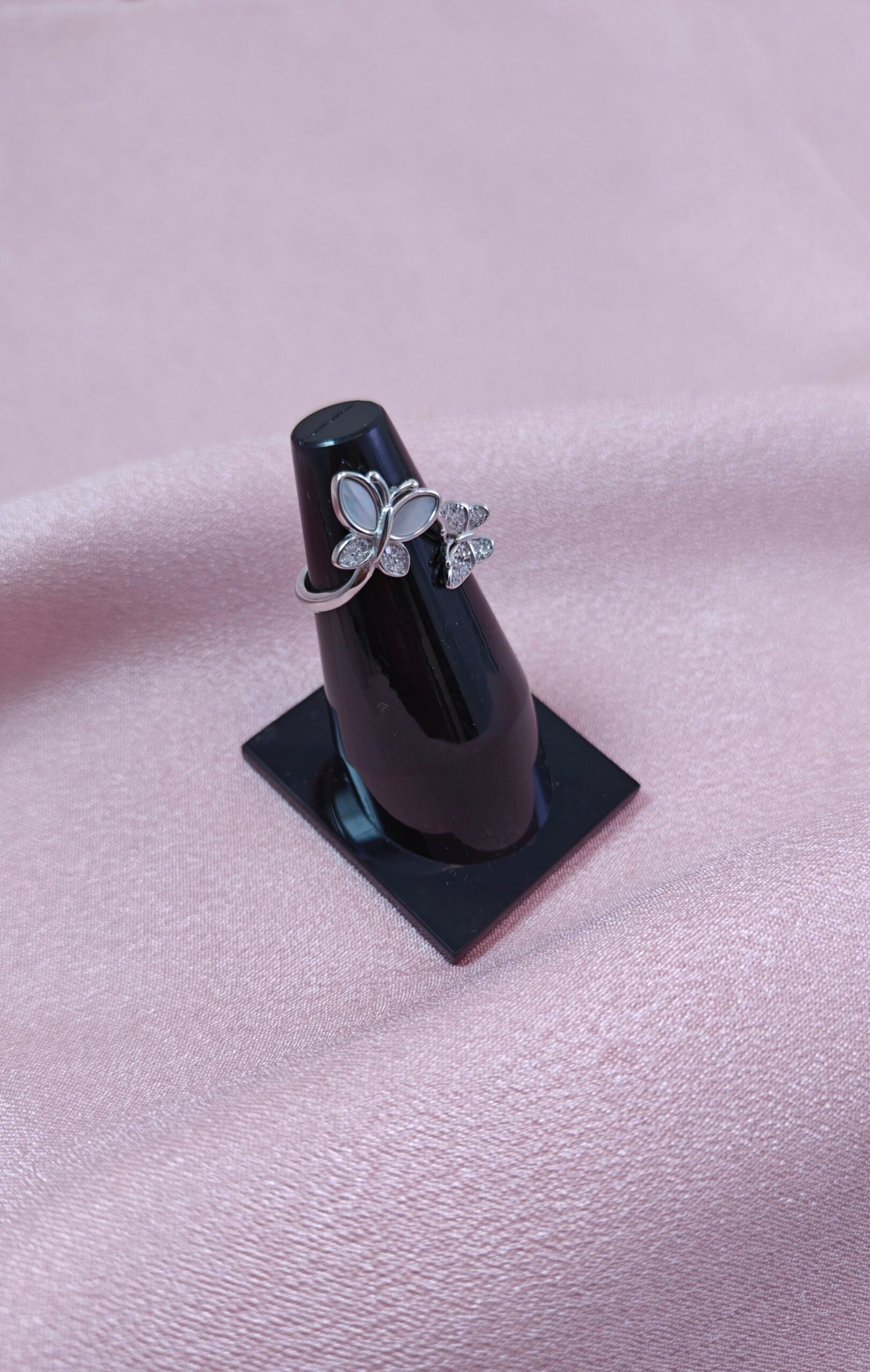 Silver ring with a flower design on a black stand against a pink fabric background