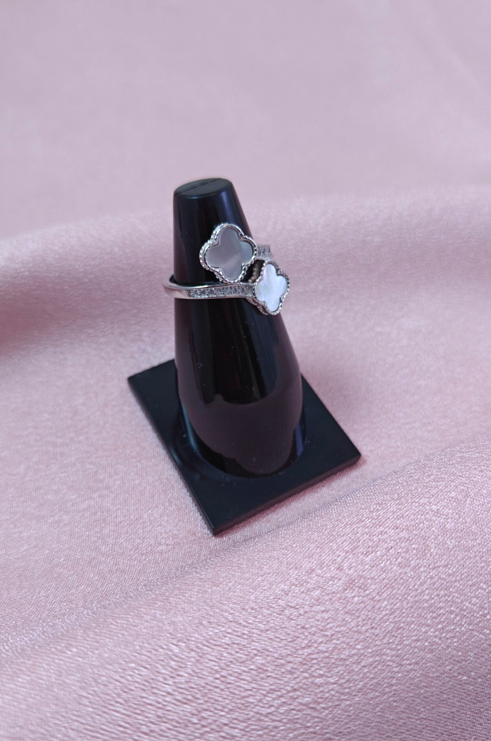 Silver ring with a heart design on a black stand against a pink fabric background