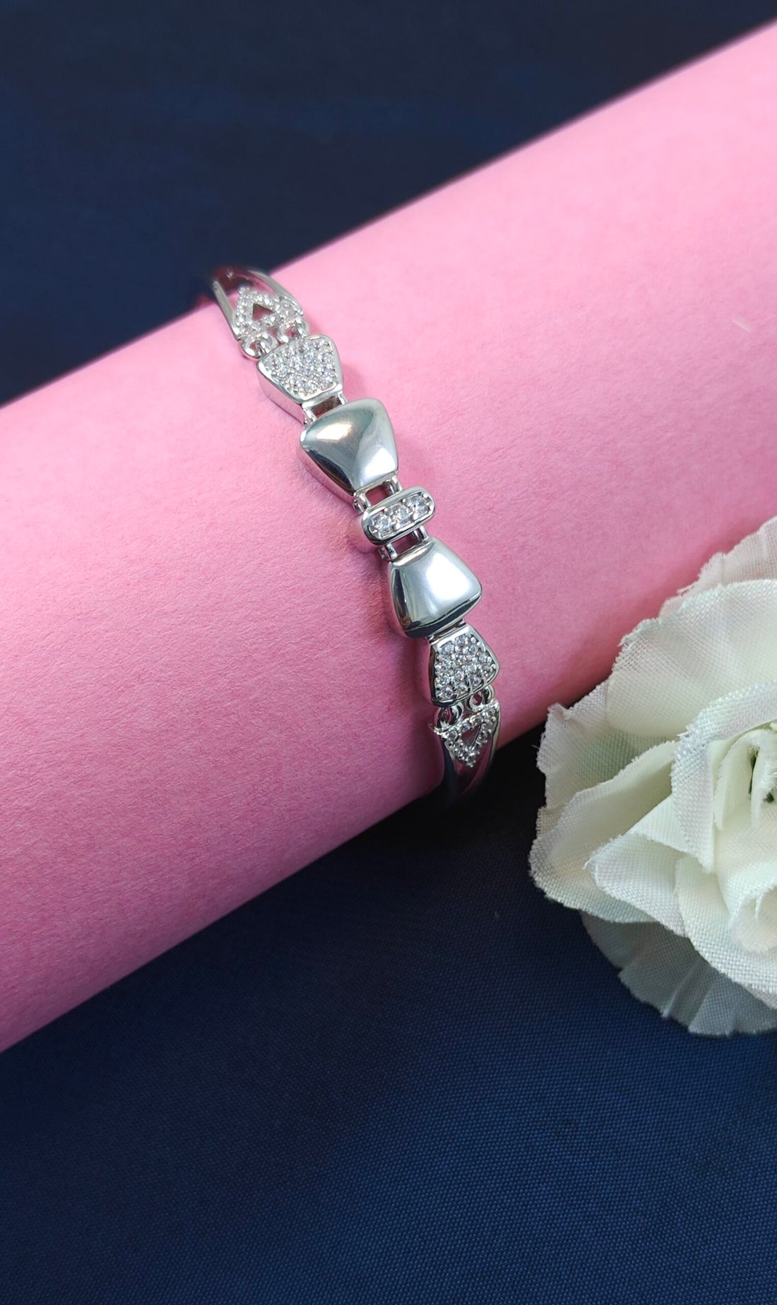 Silver bracelet with clear stones on a pink surface with a white flower