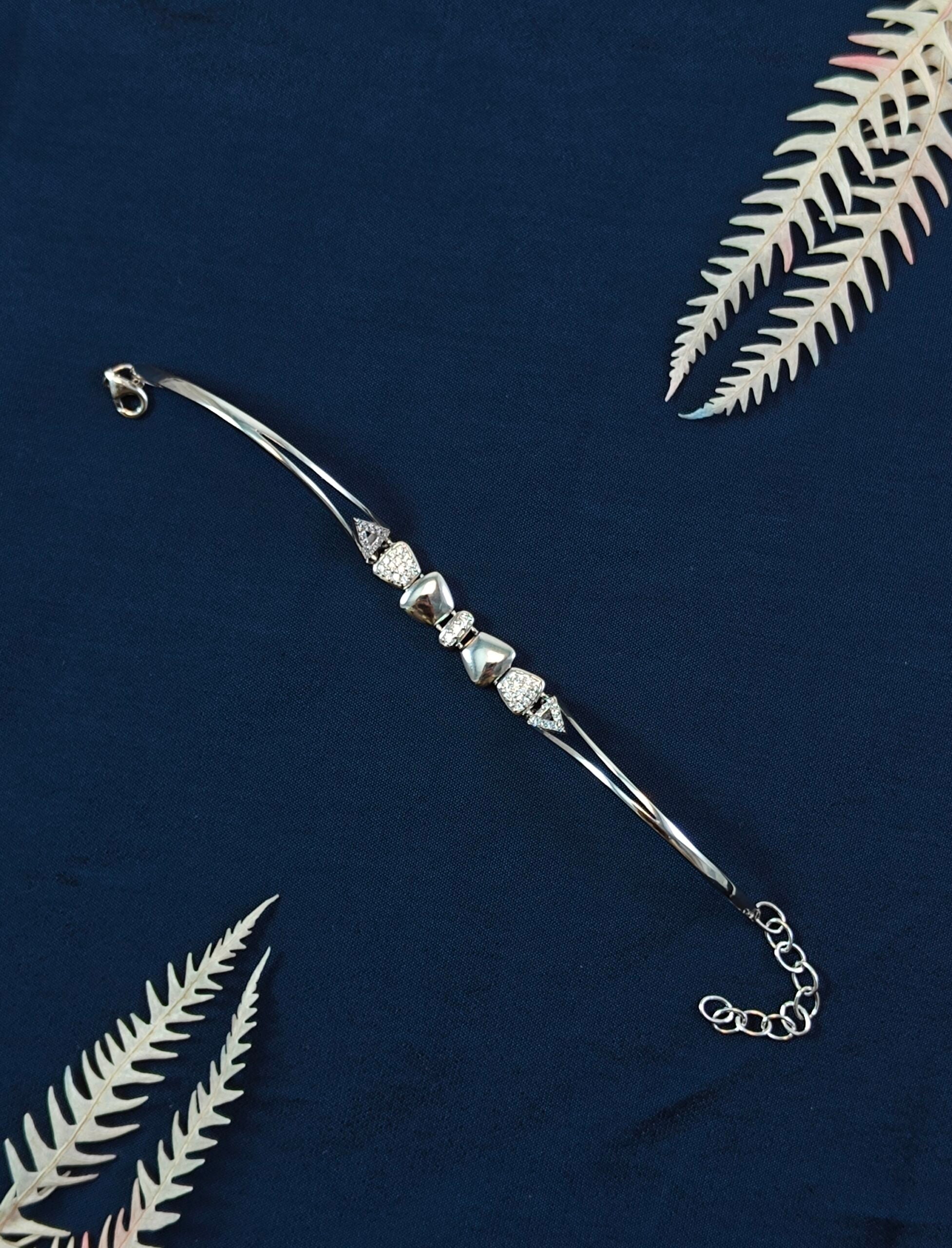 Silver bracelet with decorative elements on a dark blue background with white leaves.