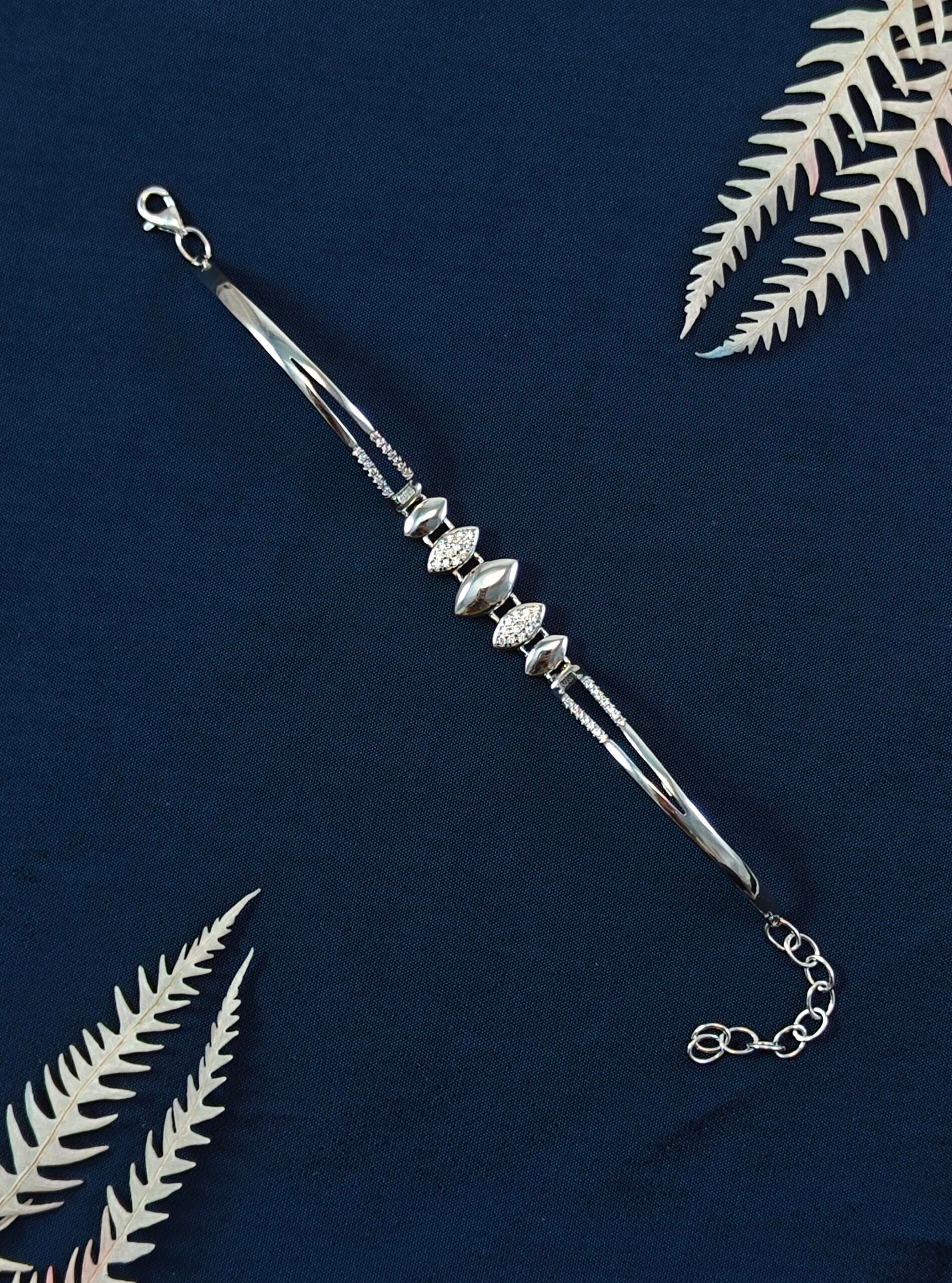 Silver bracelet with decorative elements on a dark blue background with white leaves.
