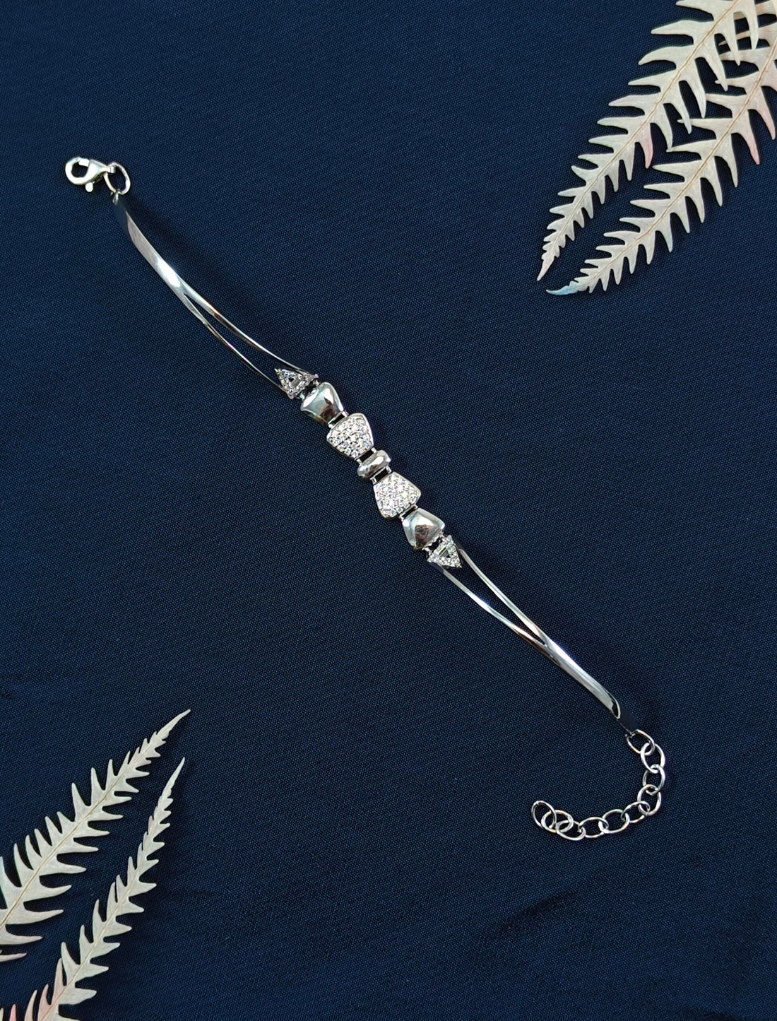 Silver bracelet with beads on a dark blue background with fern leaves