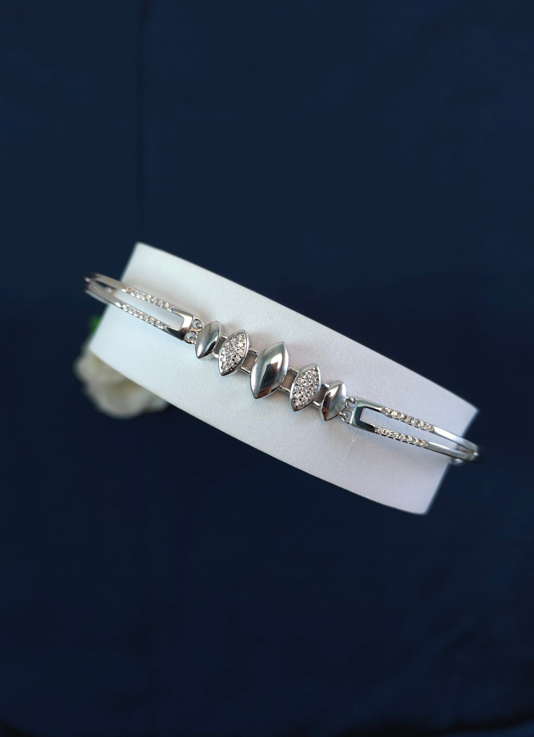 Silver bracelet with heart-shaped stones on a white card against a dark background