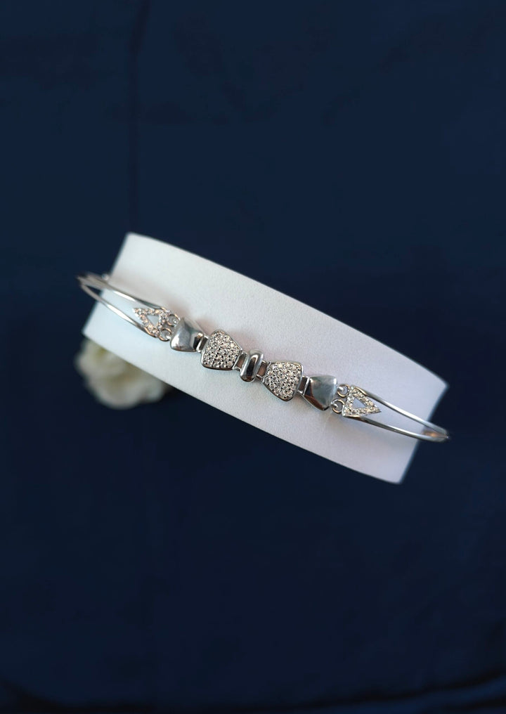 Silver bracelet with heart-shaped charms on a white leather strap against a dark background