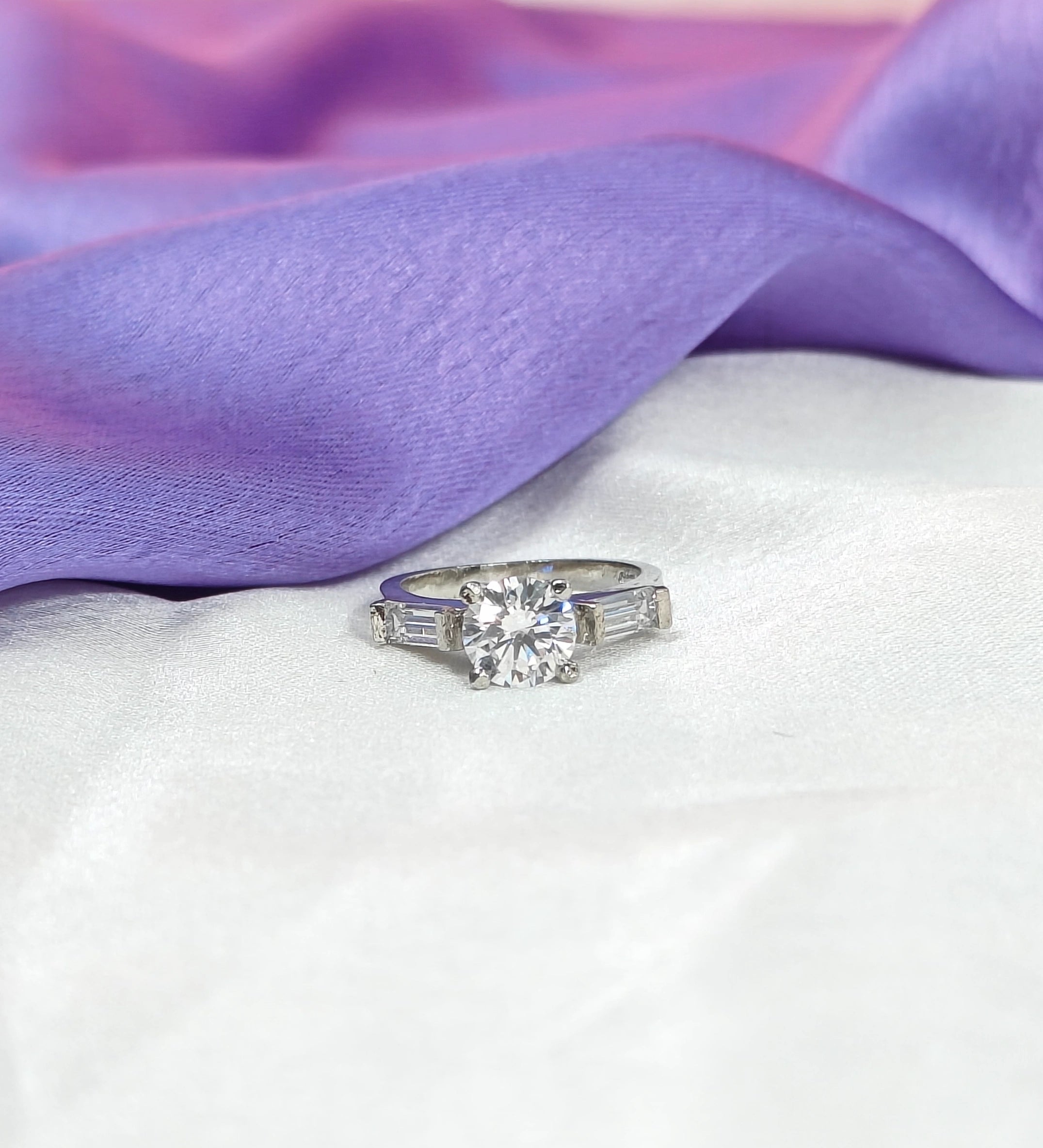 Diamond ring on a white surface with purple fabric in the background