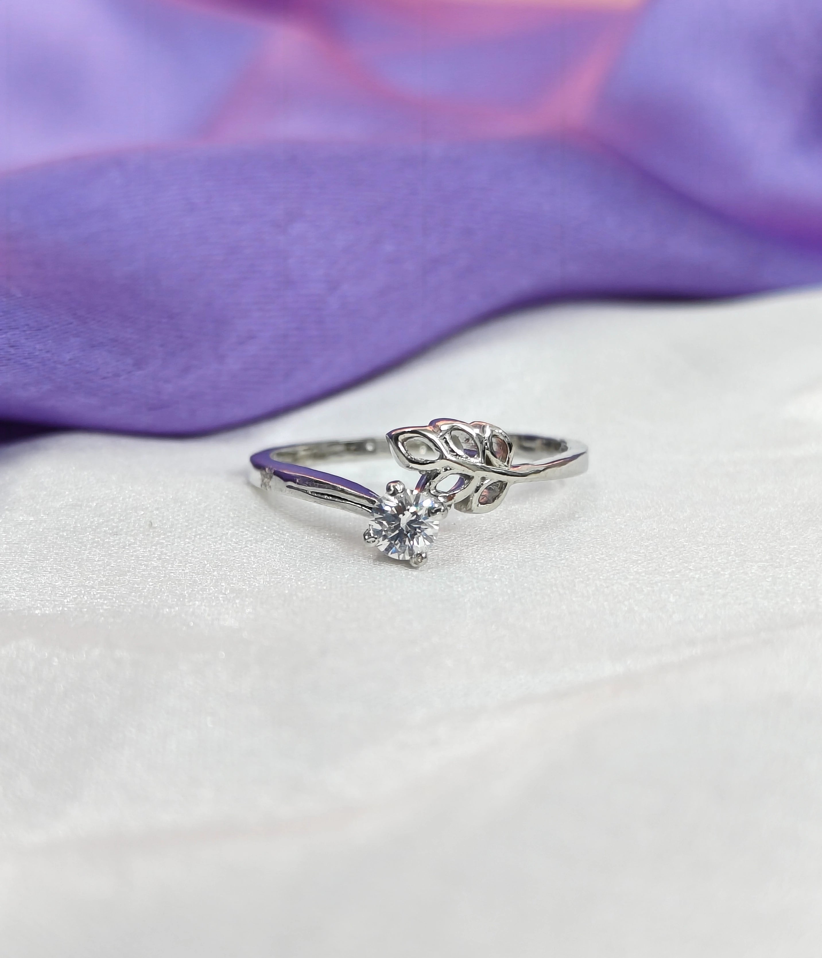 Silver ring with a diamond on a white surface with purple fabric in the background