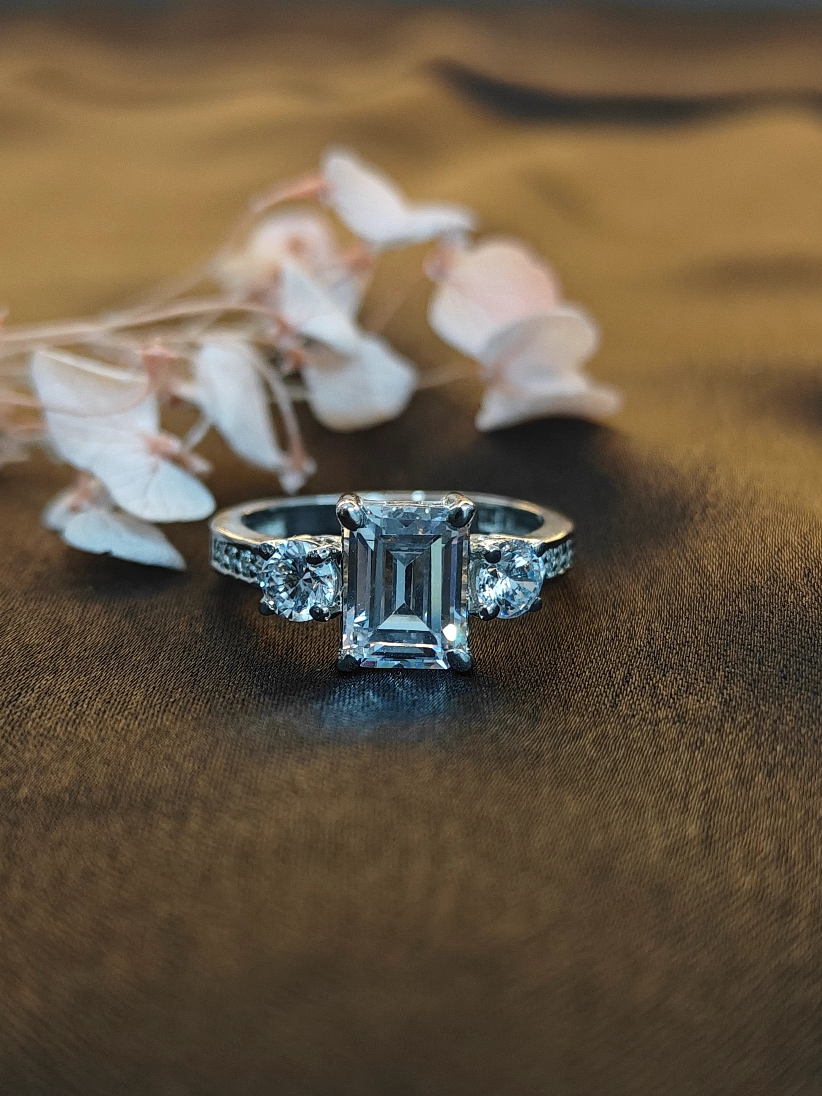 Diamond ring with emerald-cut center stone on a brown fabric background