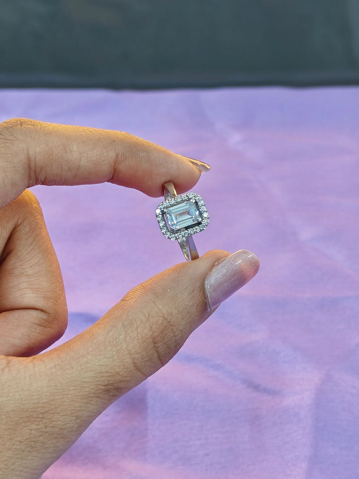 Hand holding a ring with a green gemstone against a blurred background