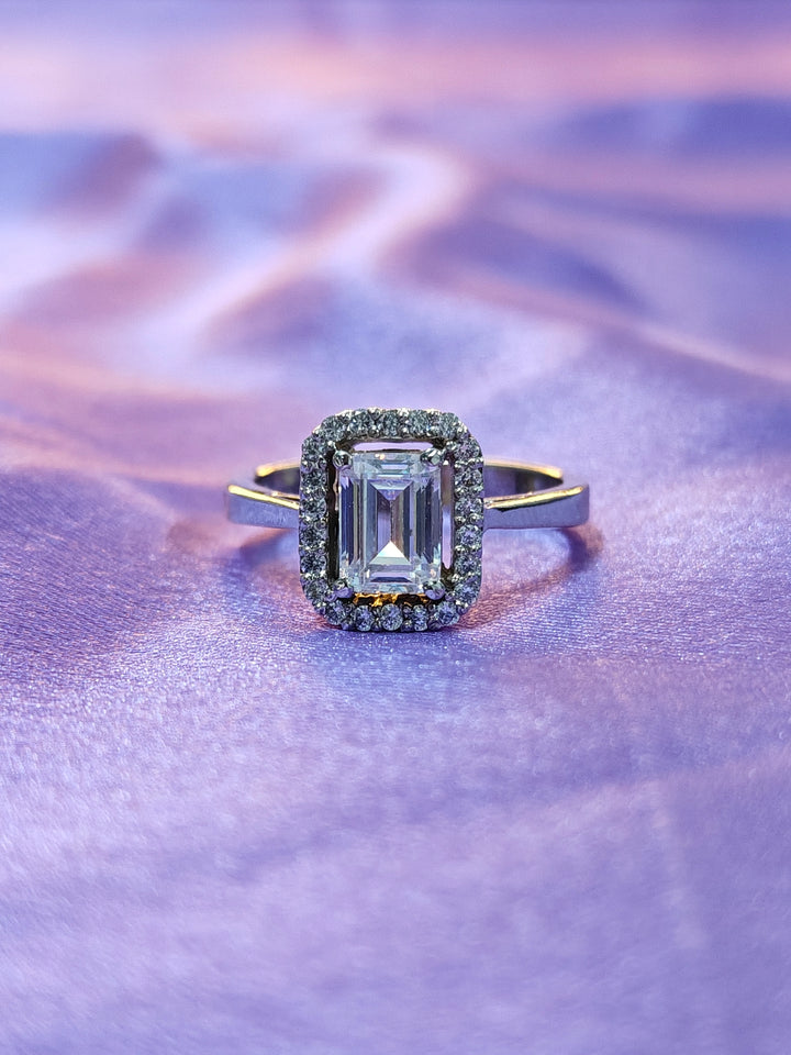 Diamond ring with emerald-cut center stone on a purple textured background