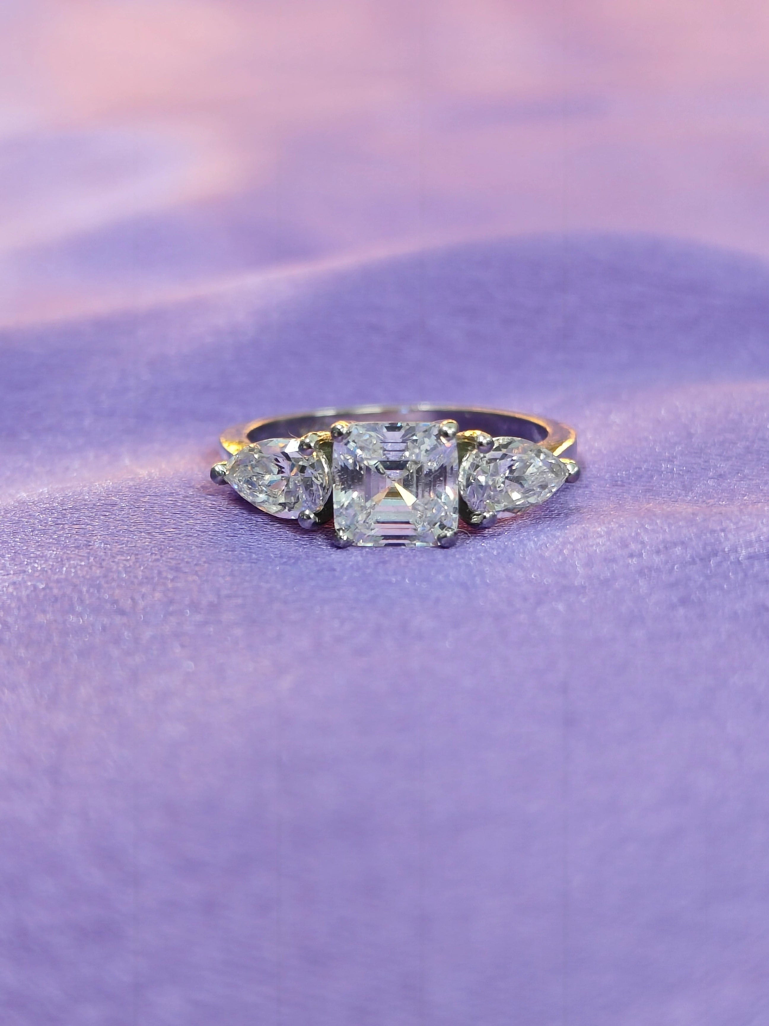 Diamond ring with three pear-shaped stones on a purple fabric background