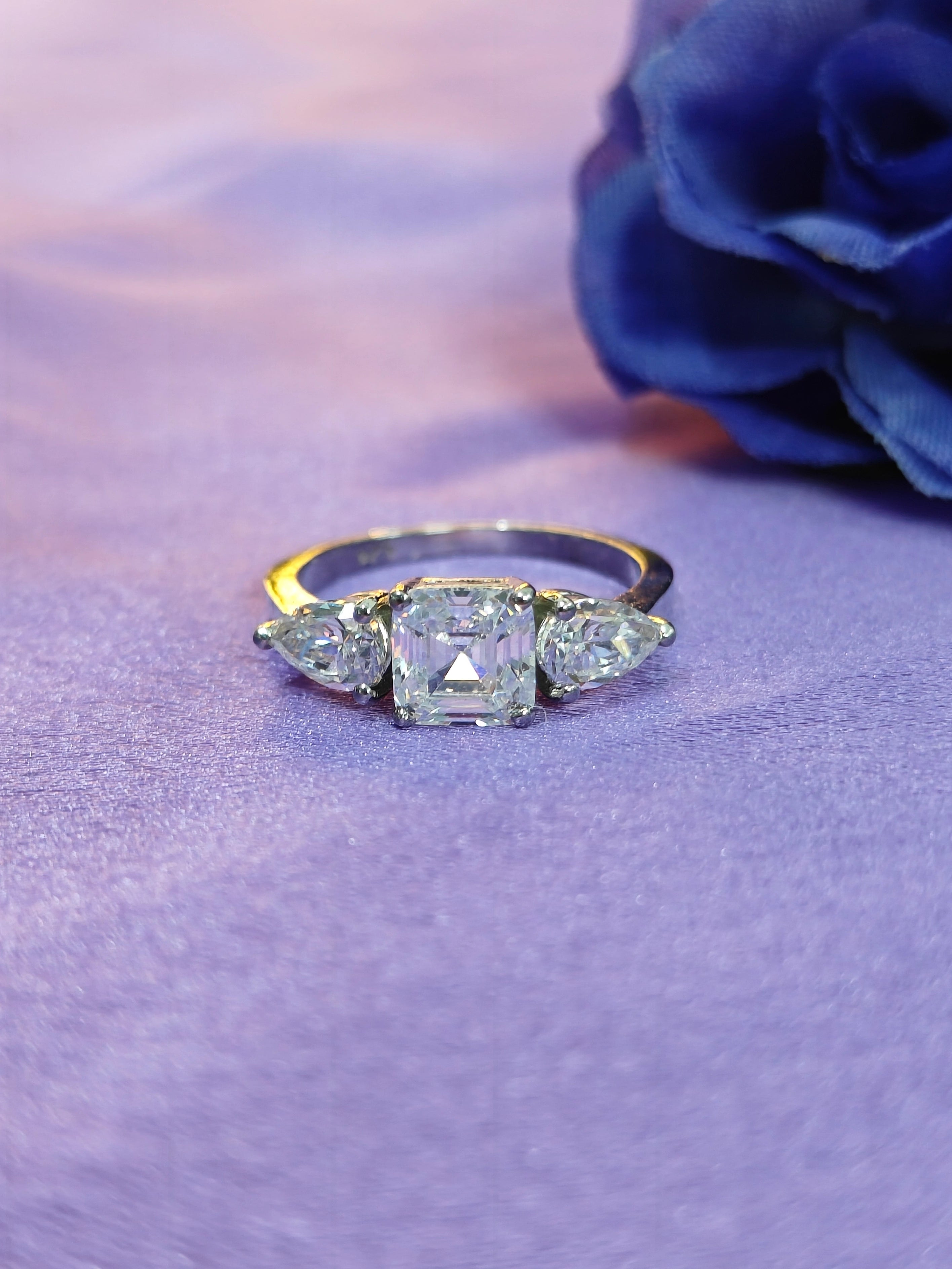 Diamond ring with three stones on a purple surface with a blue flower.