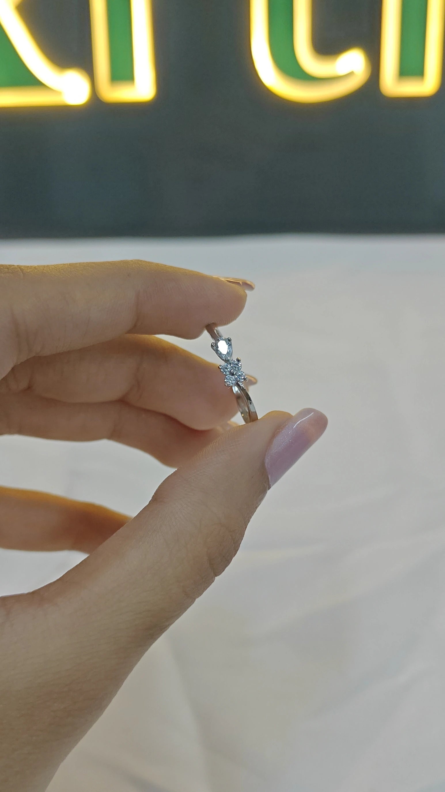 Hand holding a diamond ring with a blurred neon sign in the background