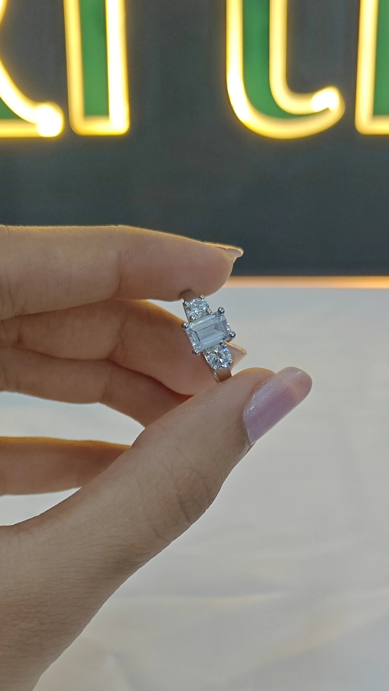 Diamond ring held by a hand with a blurred neon sign in the background