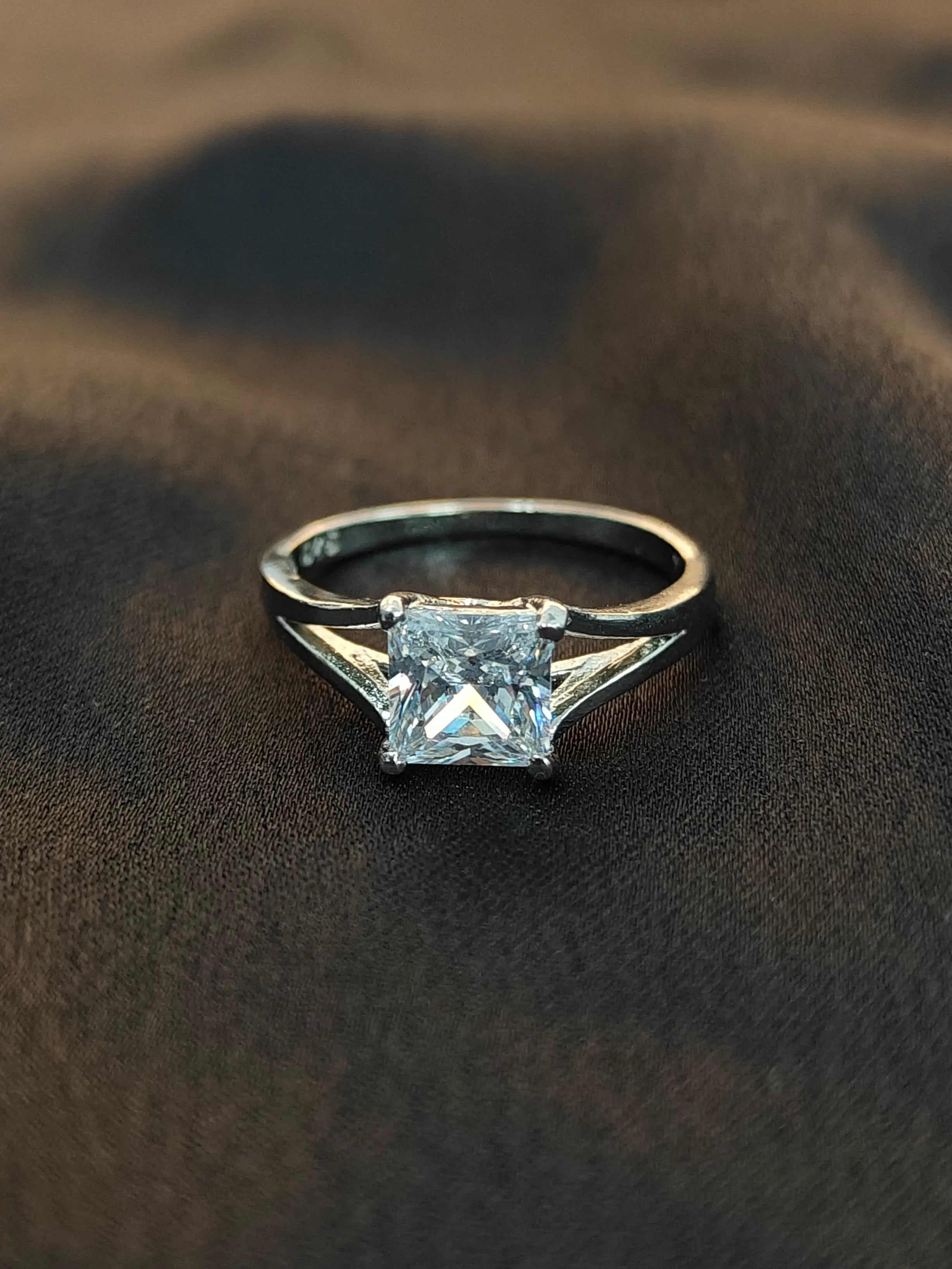 Silver ring with a square-cut gemstone on a brown fabric background