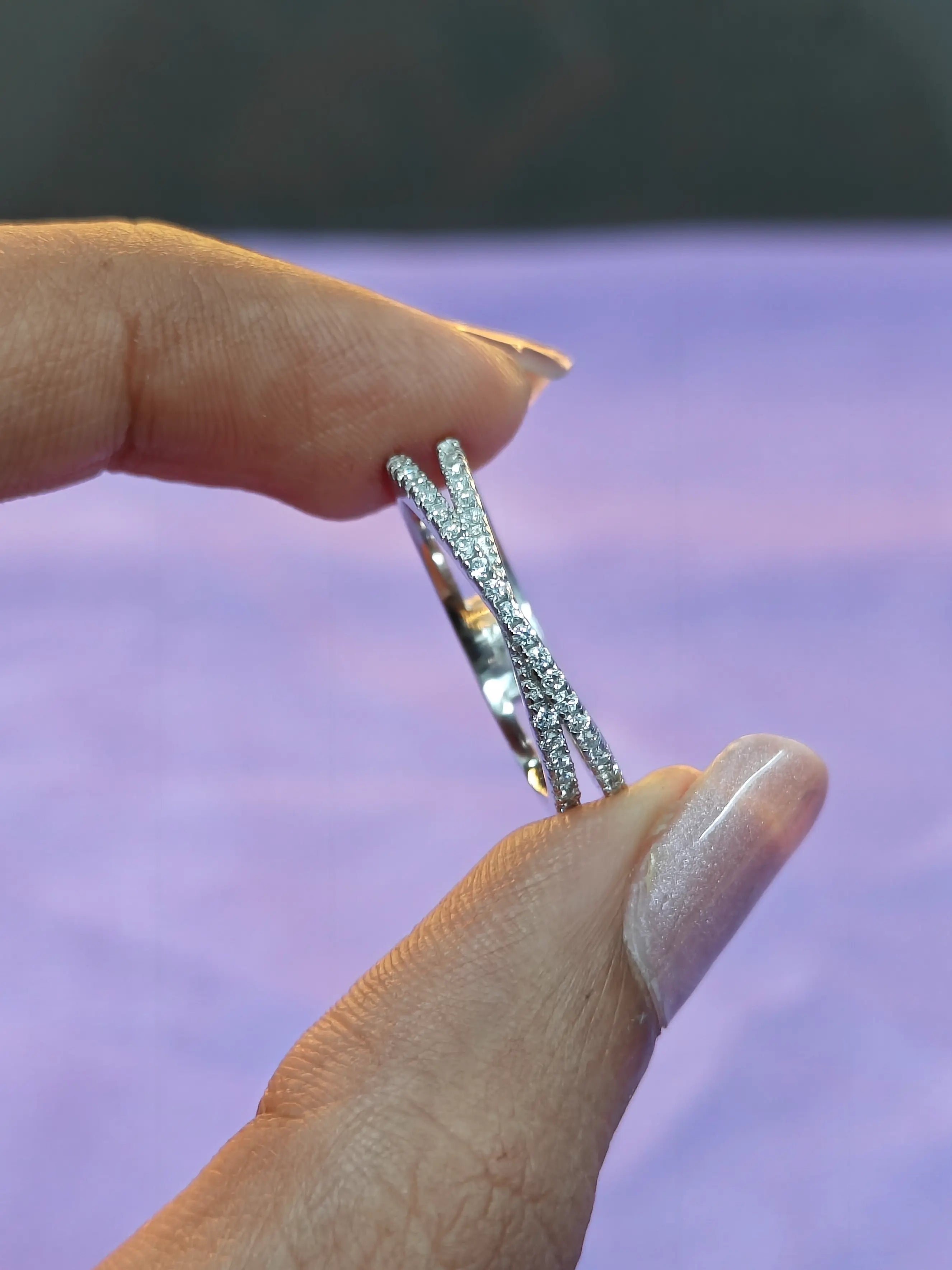 Hand holding two silver rings against a blurred purple background