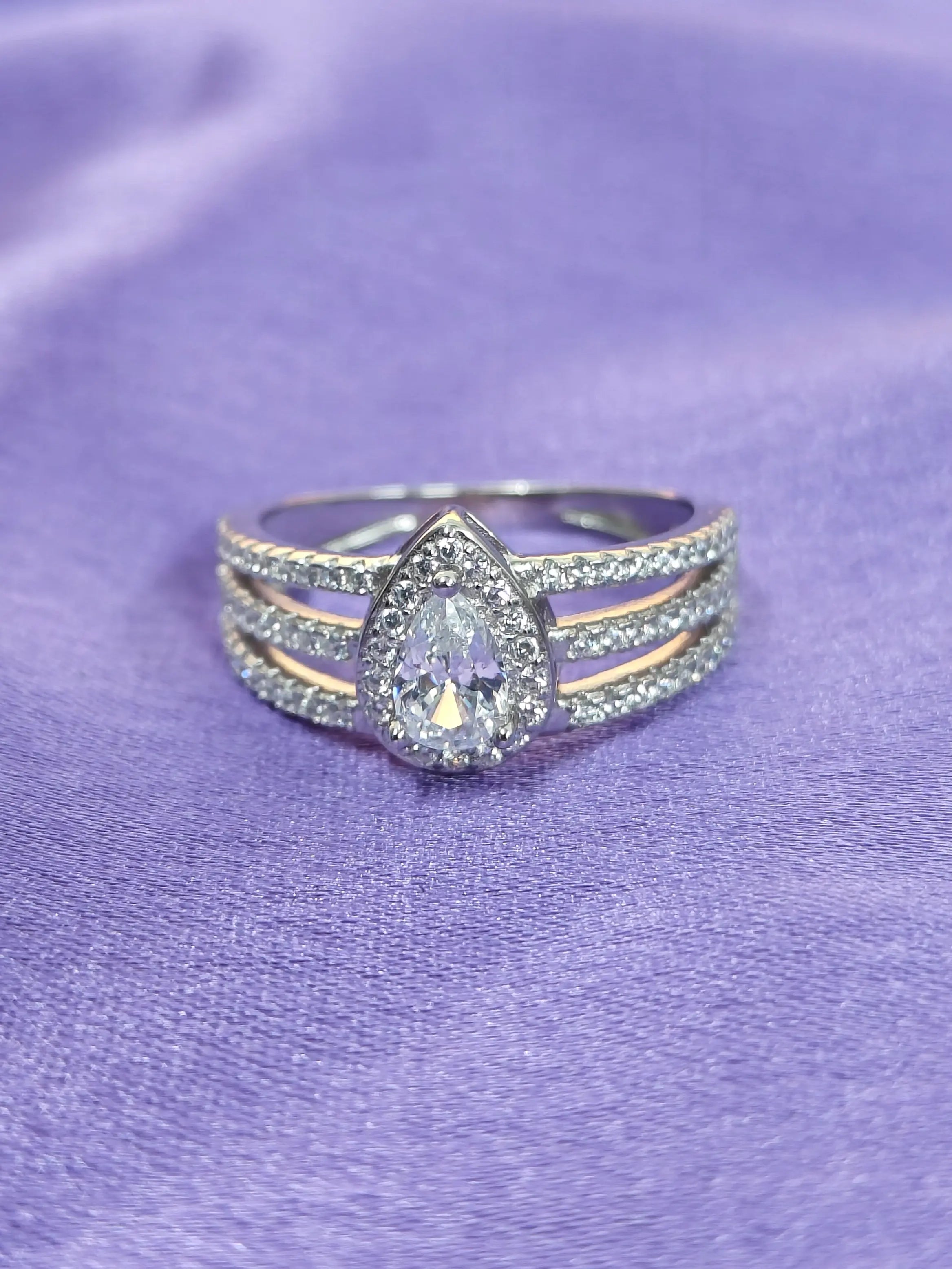 Silver ring with a teardrop-shaped diamond on a purple fabric background