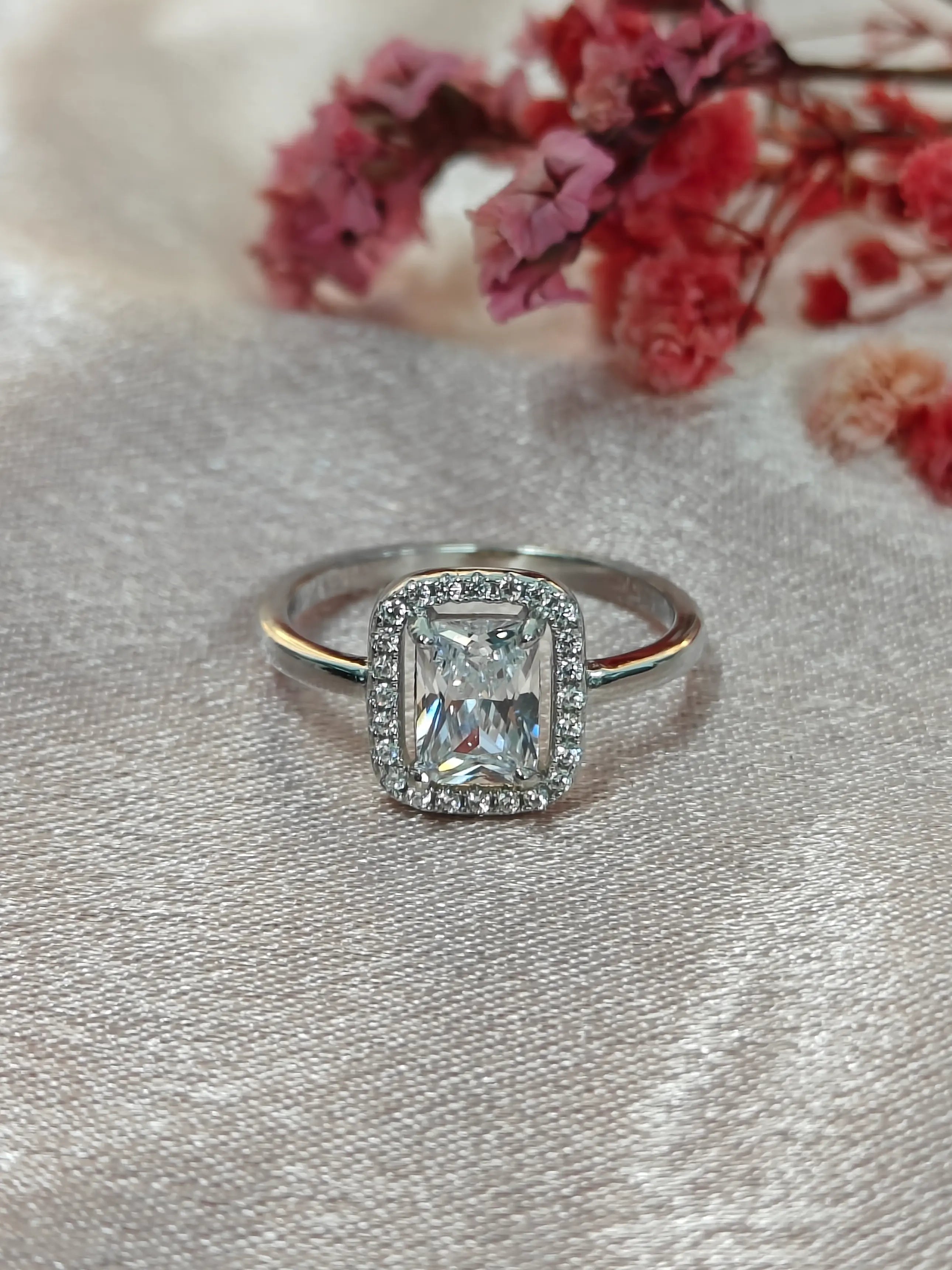 Silver ring with a diamond on a textured surface with pink flowers in the background