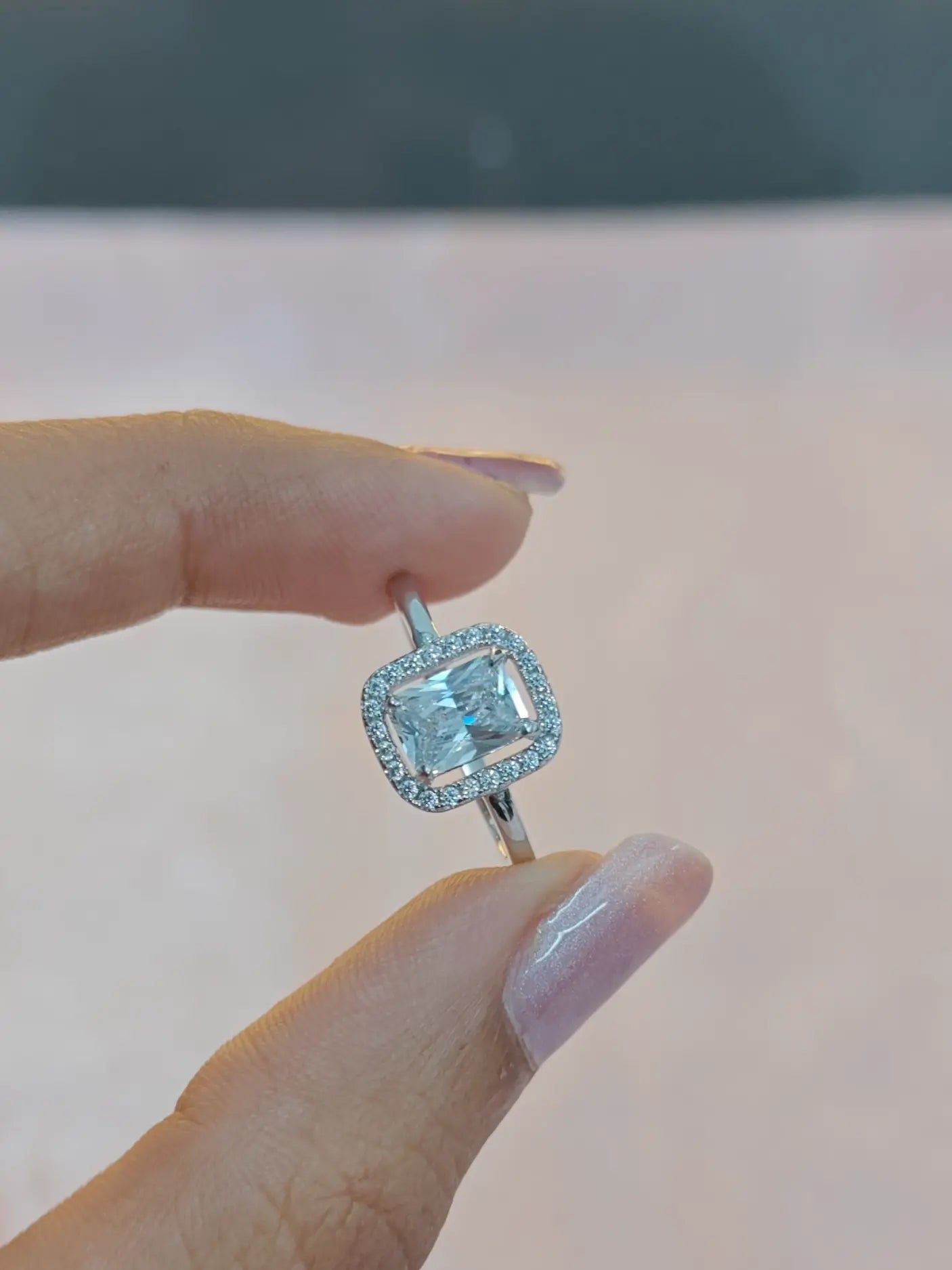 Silver ring with a blue gemstone held between two fingers against a neutral background