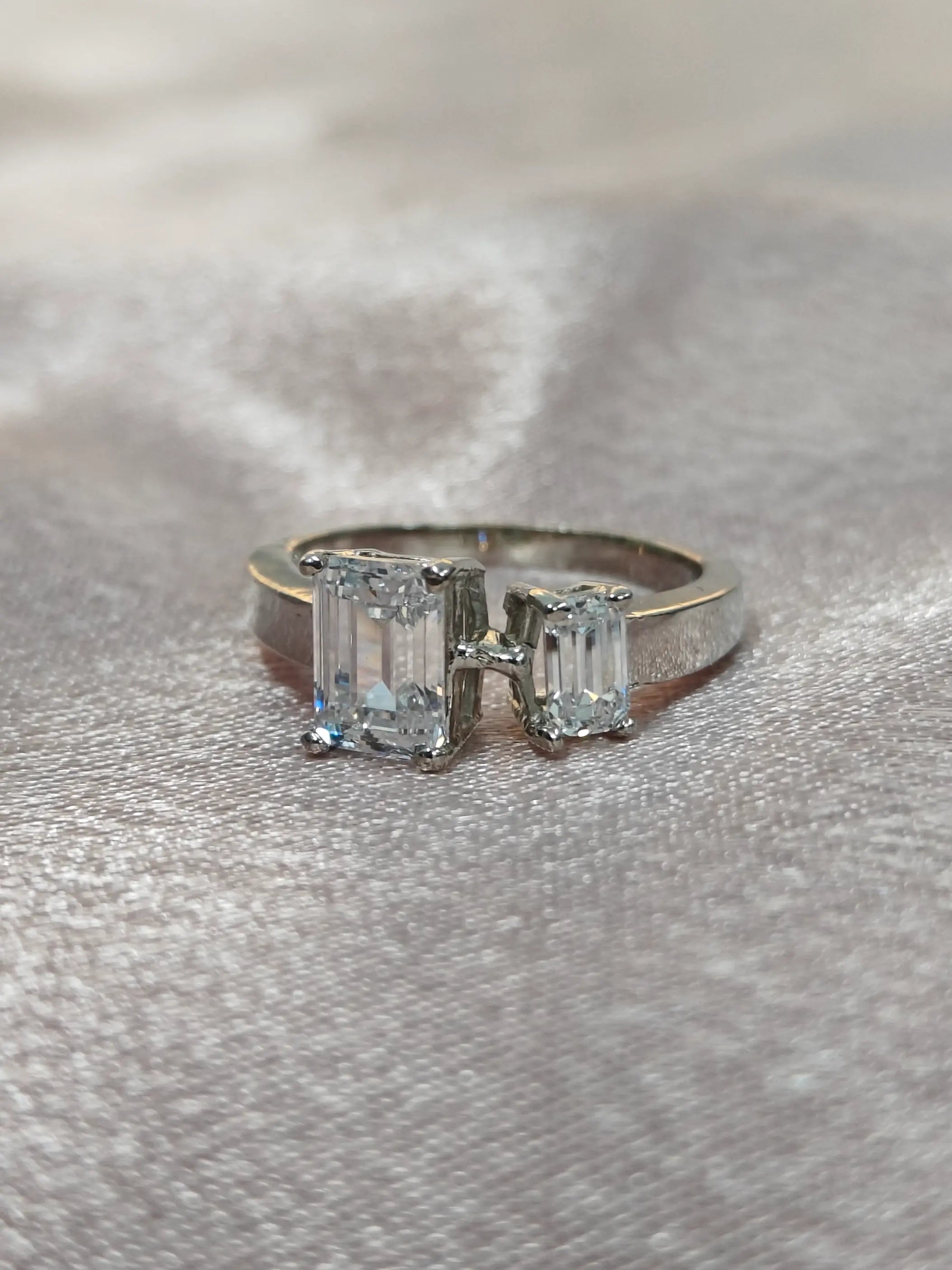 Diamond ring with emerald-cut stones on a gray fabric background