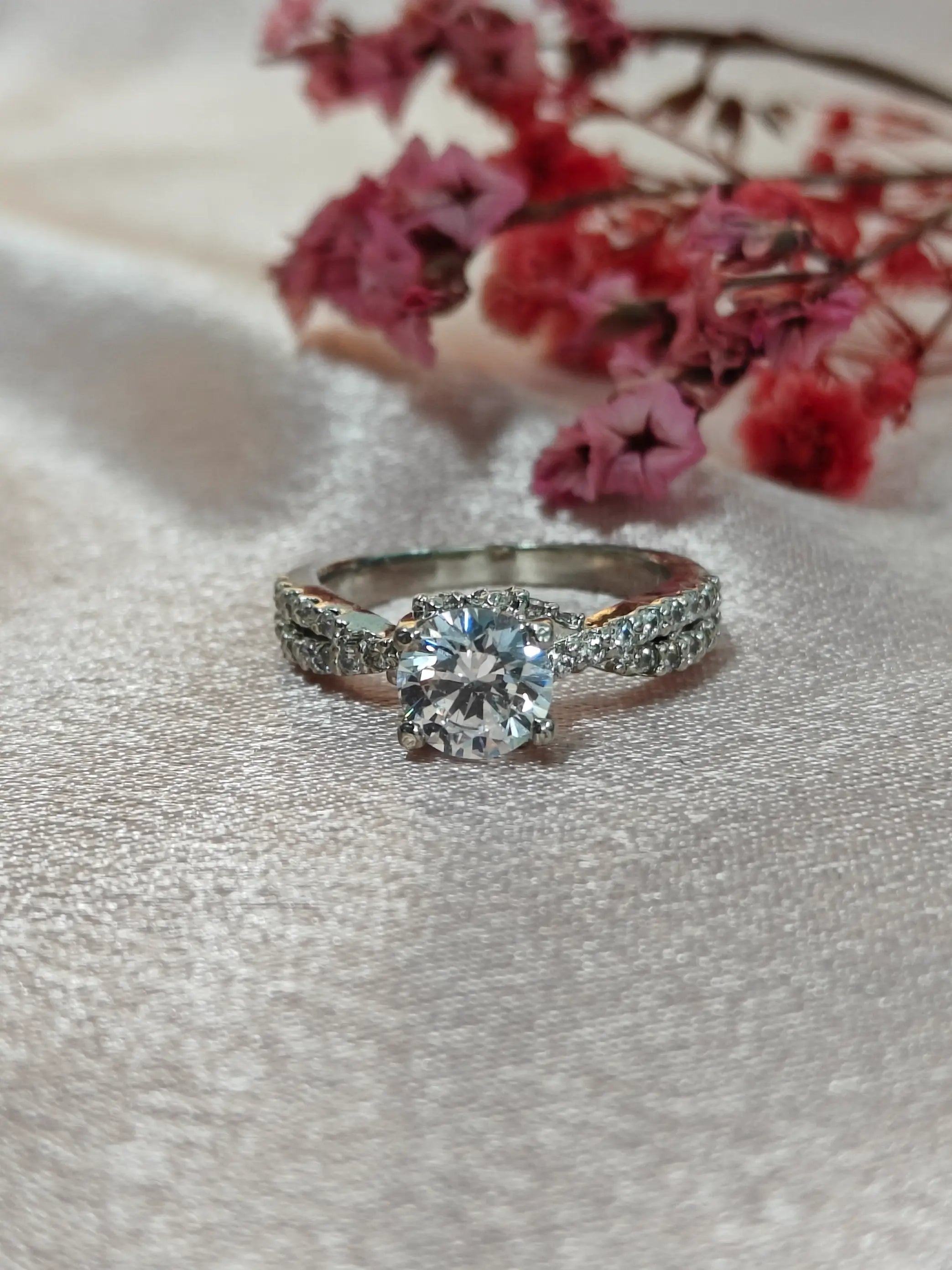 Diamond ring on a textured surface with pink flowers in the background