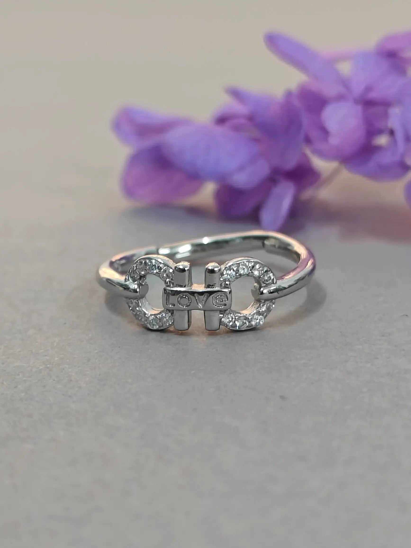 Silver ring with embedded stones on a gray surface with purple flowers in the background