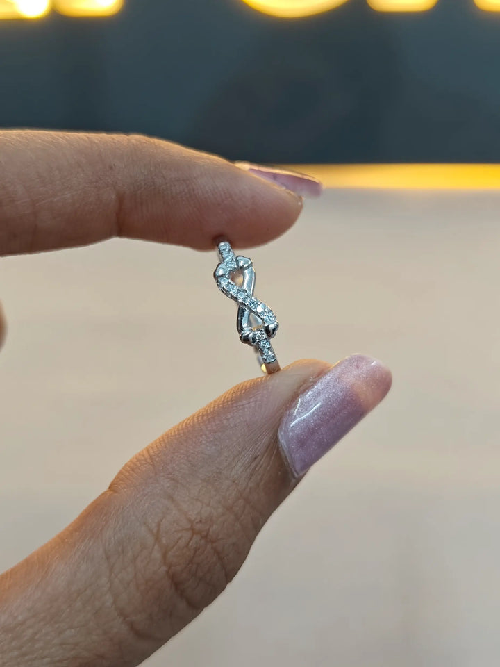 Silver ring with a unique design held between fingers against a blurred background