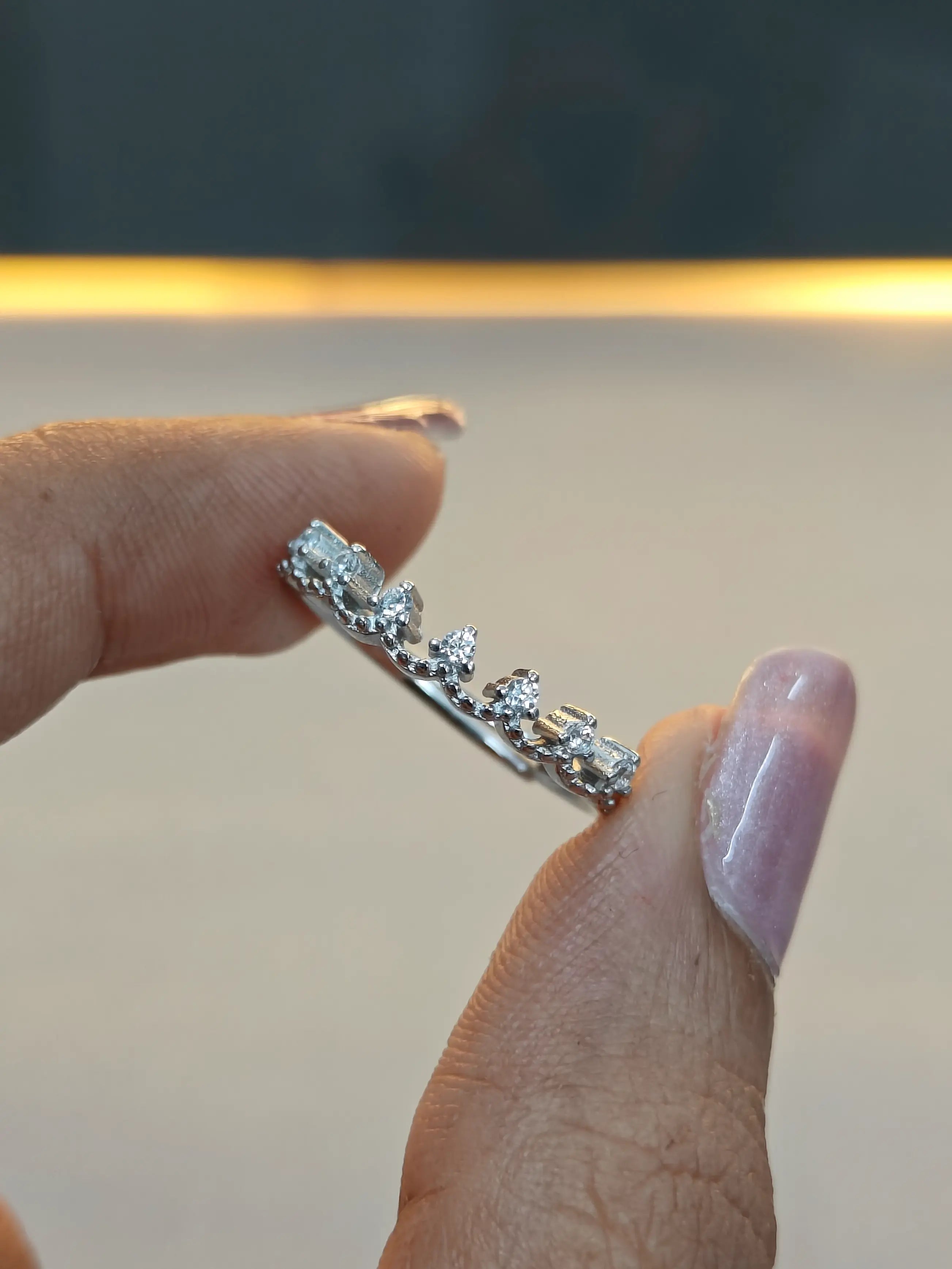 Silver ring with diamonds held between fingers against a neutral background